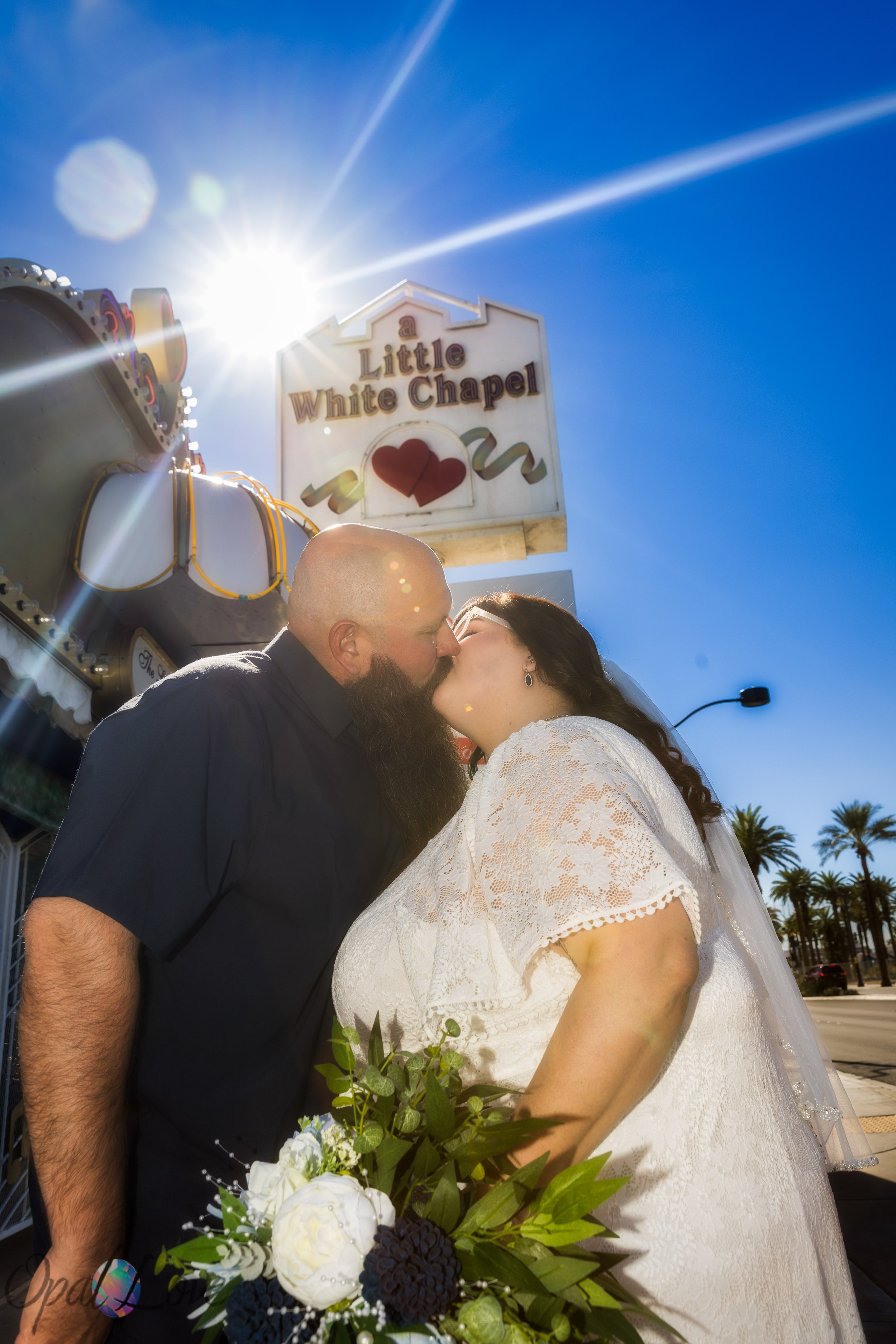 Couple sharing a kiss with bright sun flare and the Little White Chapel sign behind them.