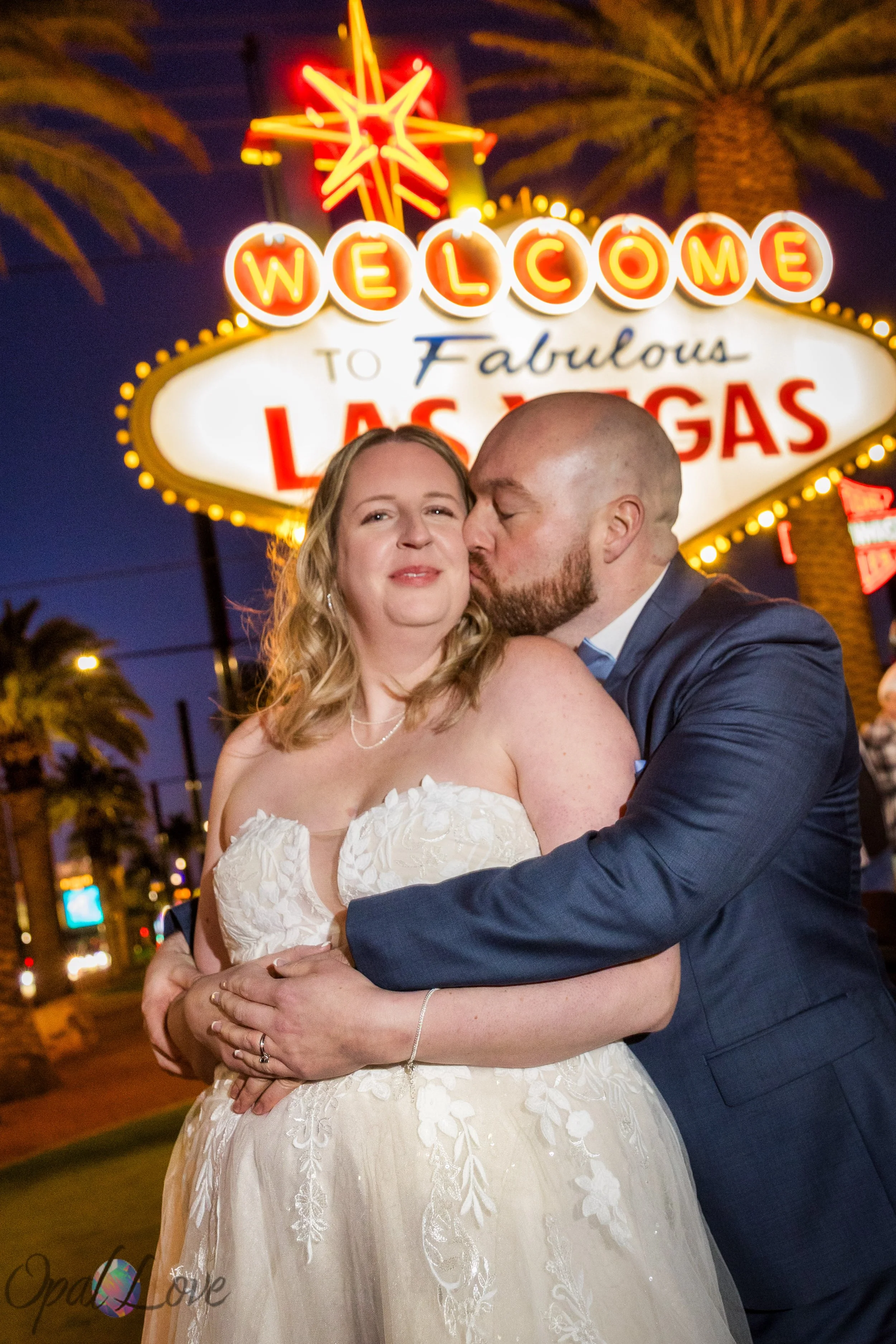 Groom kissing bride in front of the Welcome to Fabulous Las Vegas sign during a nighttime elopement photo session.