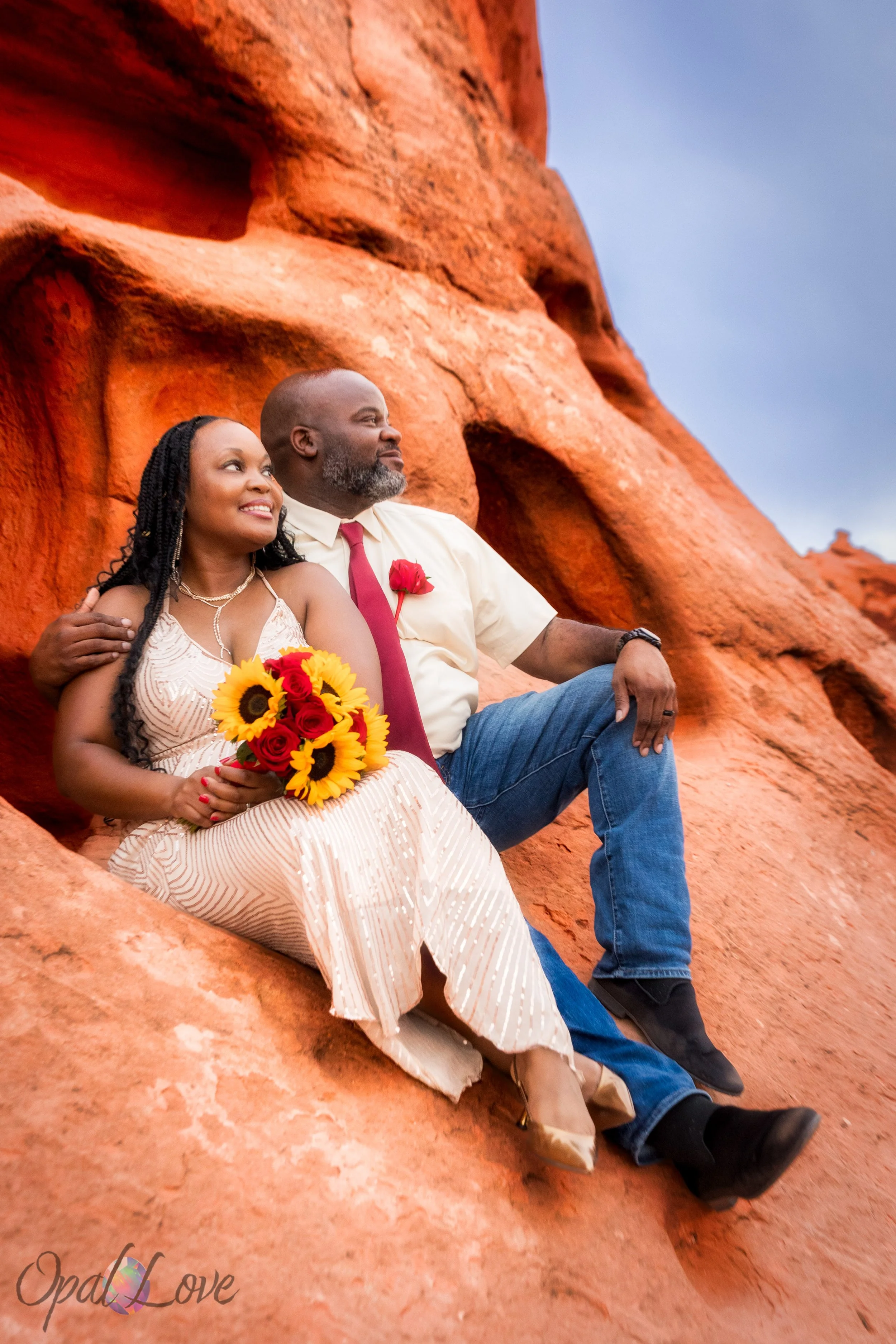 Couple sitting together on red rocks with desert landscape behind them