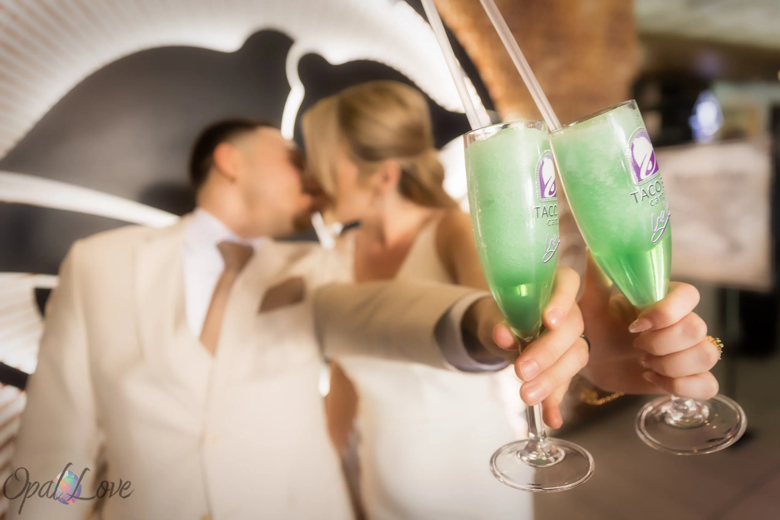 Couple kissing while holding two green champagne flutes toward the camera.