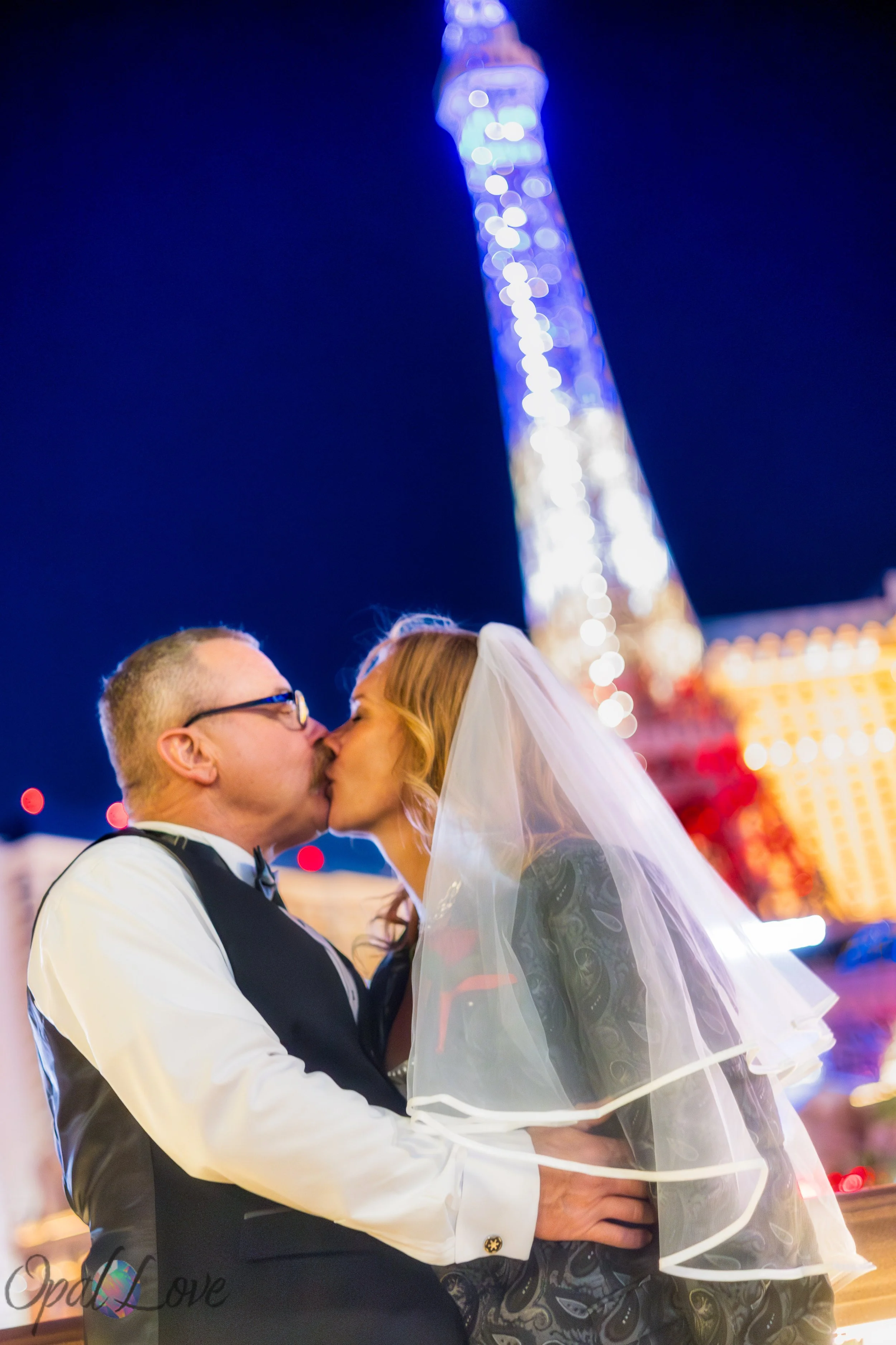 Newlyweds kissing with the illuminated Eiffel Tower at Paris Las Vegas behind them.