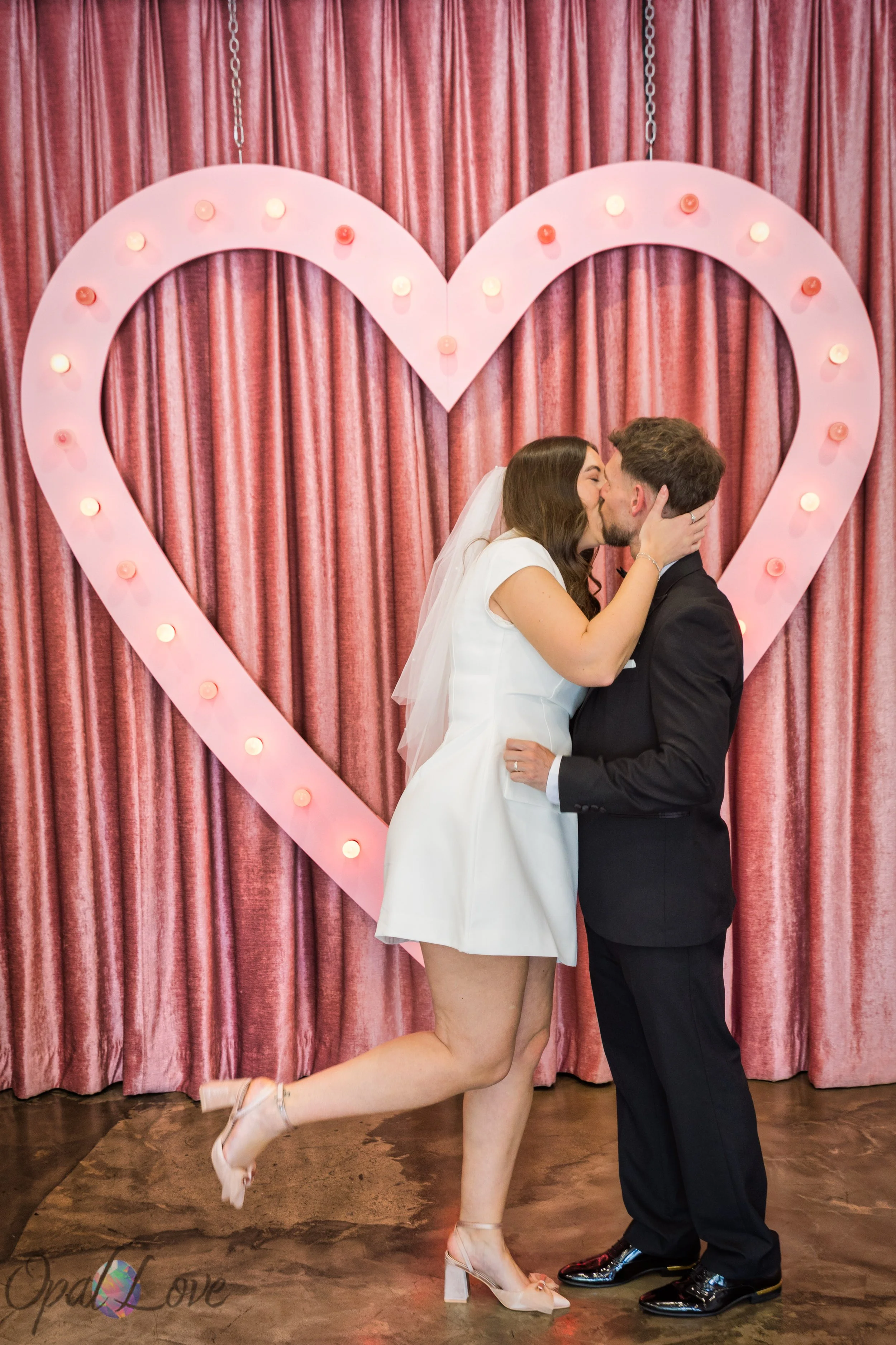 Couple kissing beneath pink heart backdrop during Las Vegas vow renewal at A Sure Thing Wedding Chapel