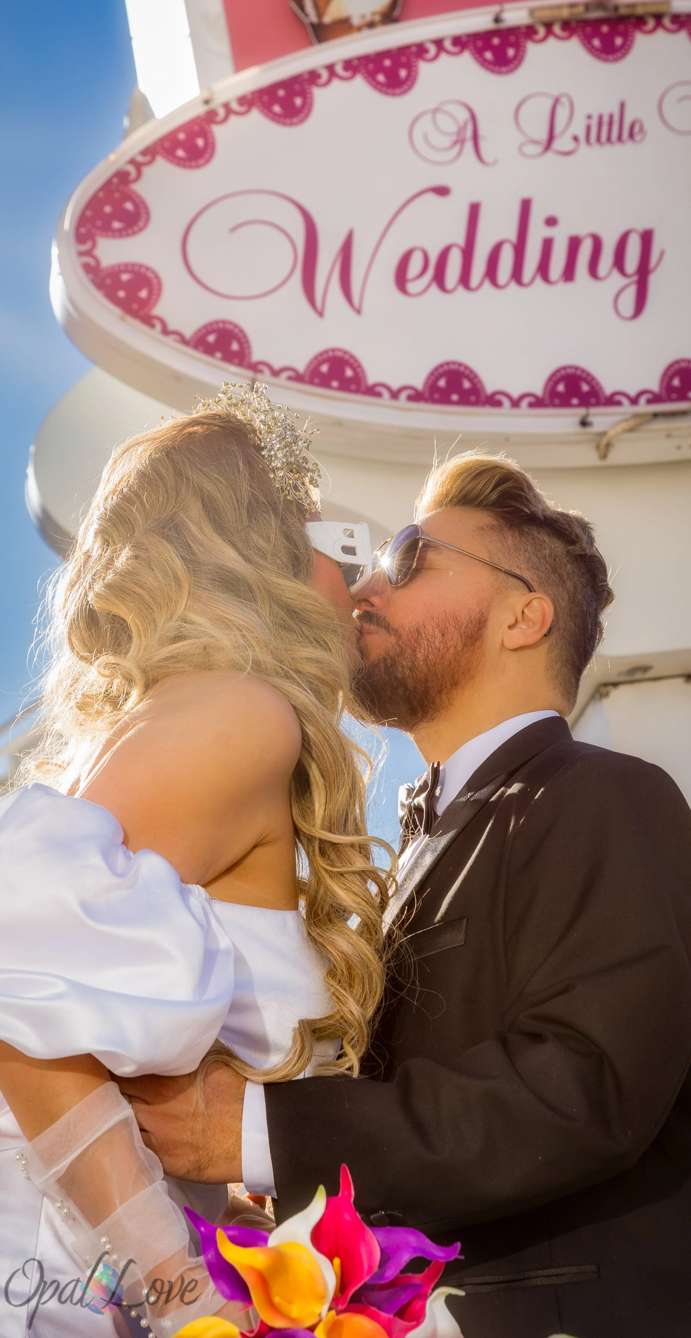 Couple kissing beneath a pink-and-white wedding chapel sign.