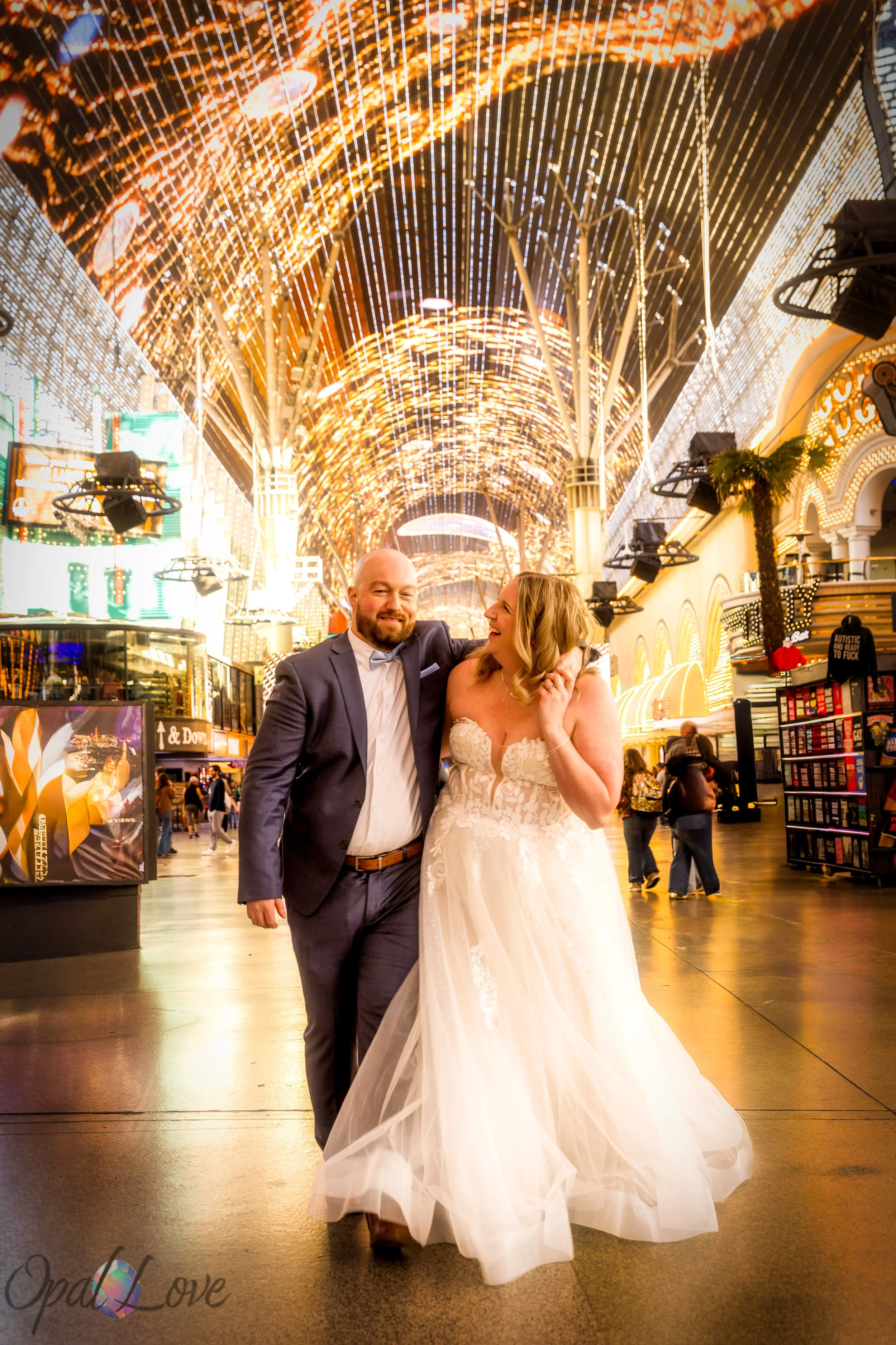 Bride and groom walking hand in hand under the glowing Fremont Street canopy during their Las Vegas elopement photo tour at night.