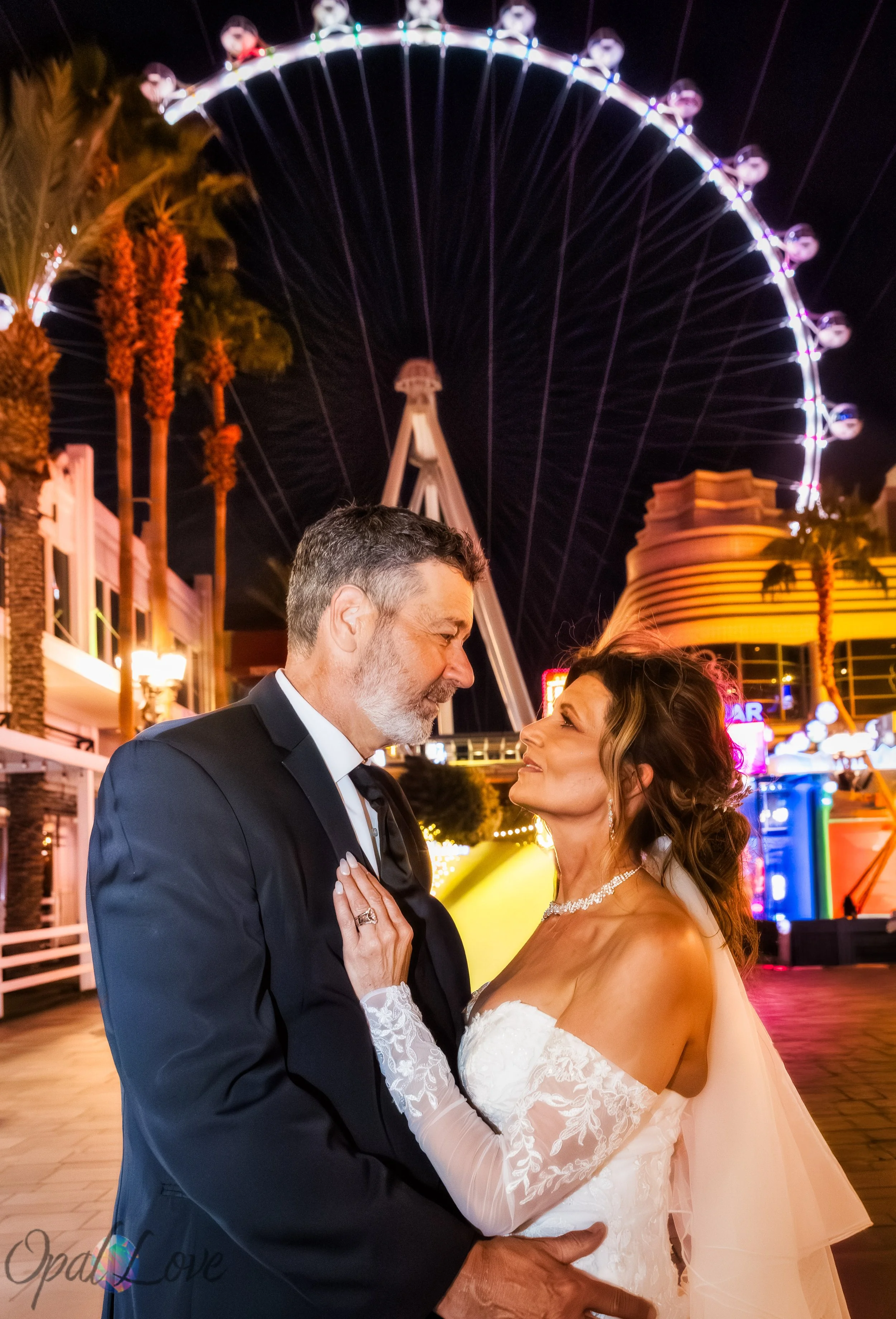 Newlyweds embrace beneath the illuminated High Roller observation wheel on the Las Vegas Strip.