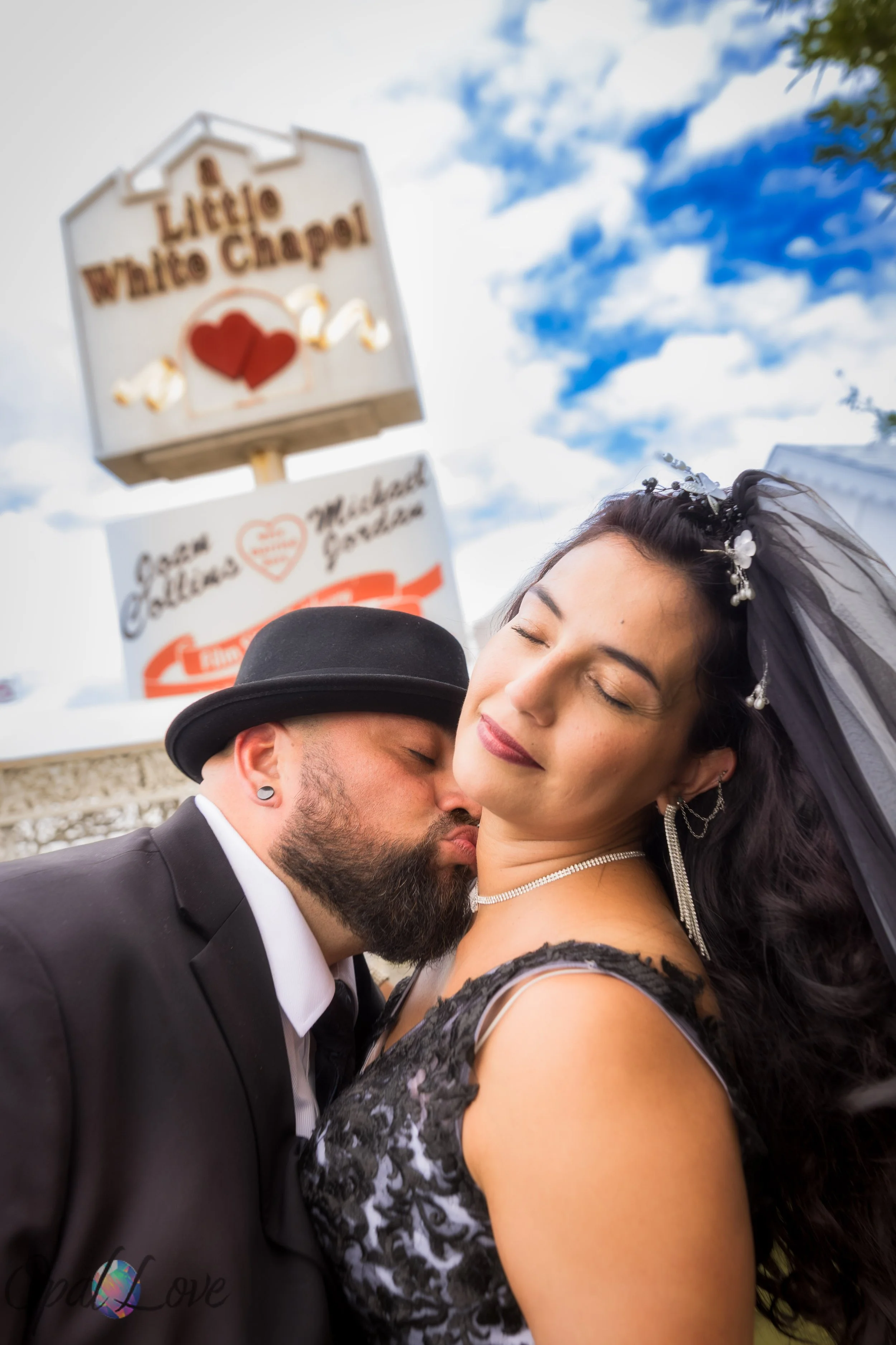 Groom kissing bride on the cheek with the Little White Chapel sign in the background.