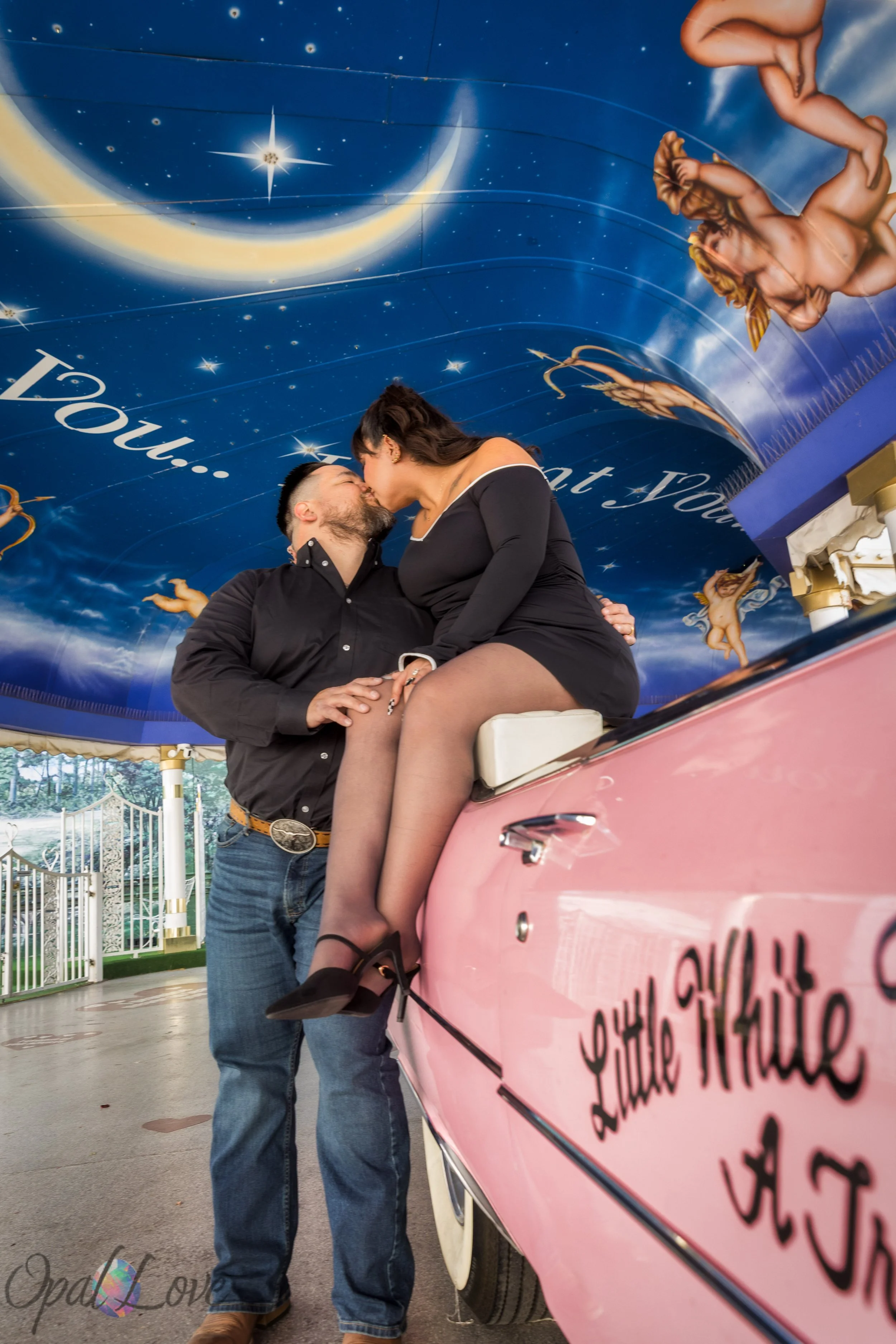 Bride and groom kissing on the pink Cadillac under the painted blue canopy at A Little White Wedding Chapel in Las Vegas.