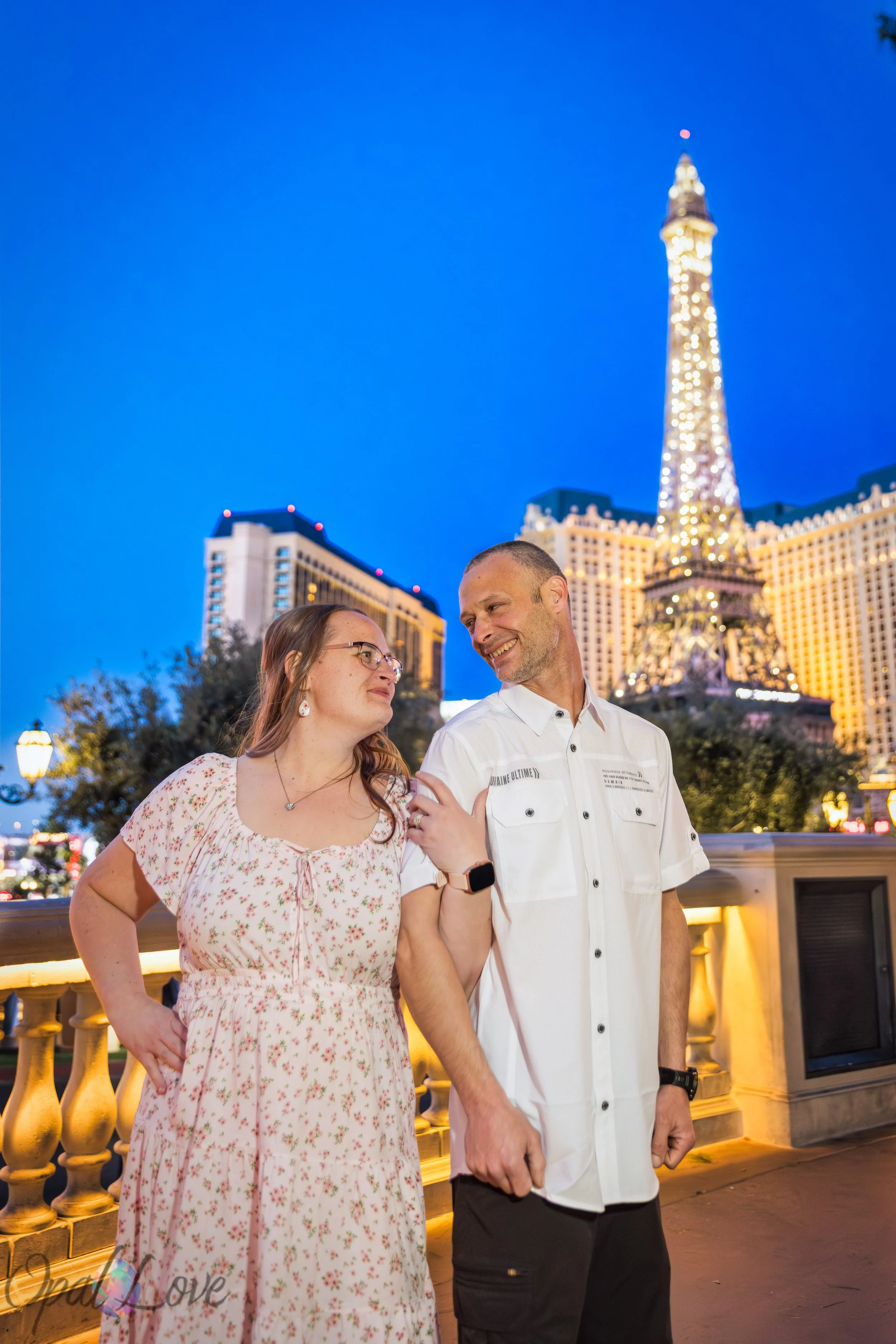 Anniversary couple standing together at Bellagio Las Vegas with Paris Las Vegas Eiffel Tower glowing in the background.