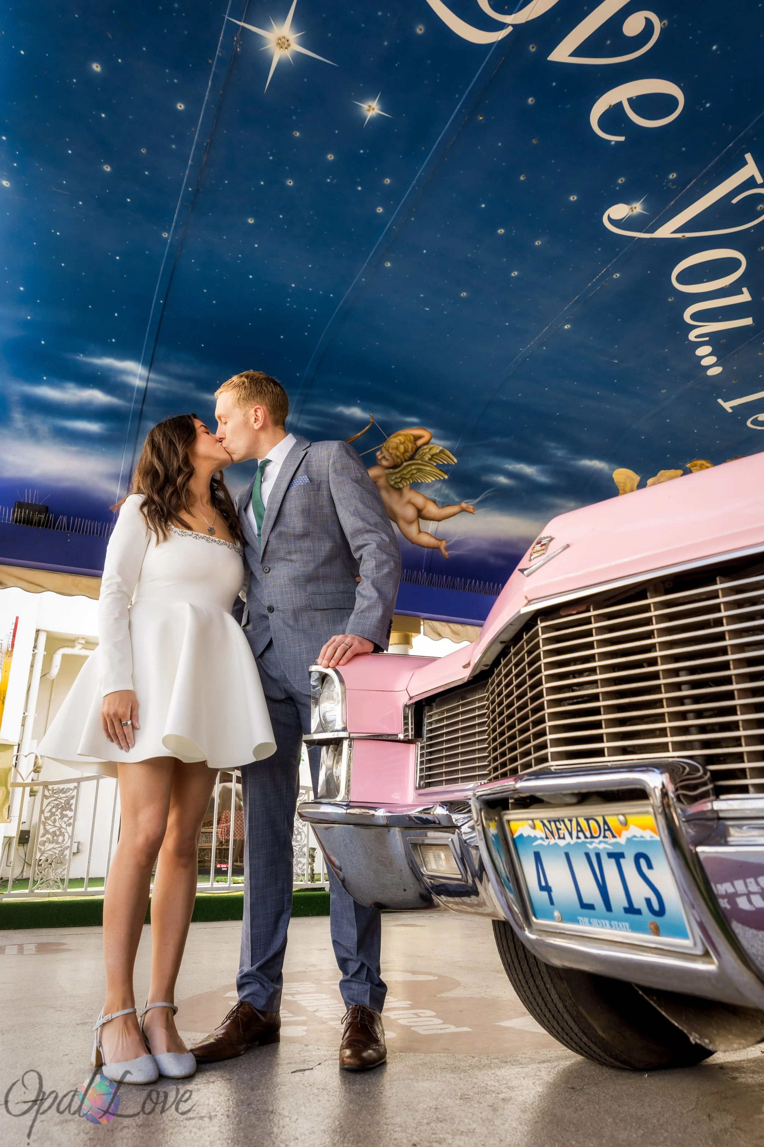 Newlyweds kissing beside the pink Cadillac under the starry blue ceiling mural at A Little White Wedding Chapel.