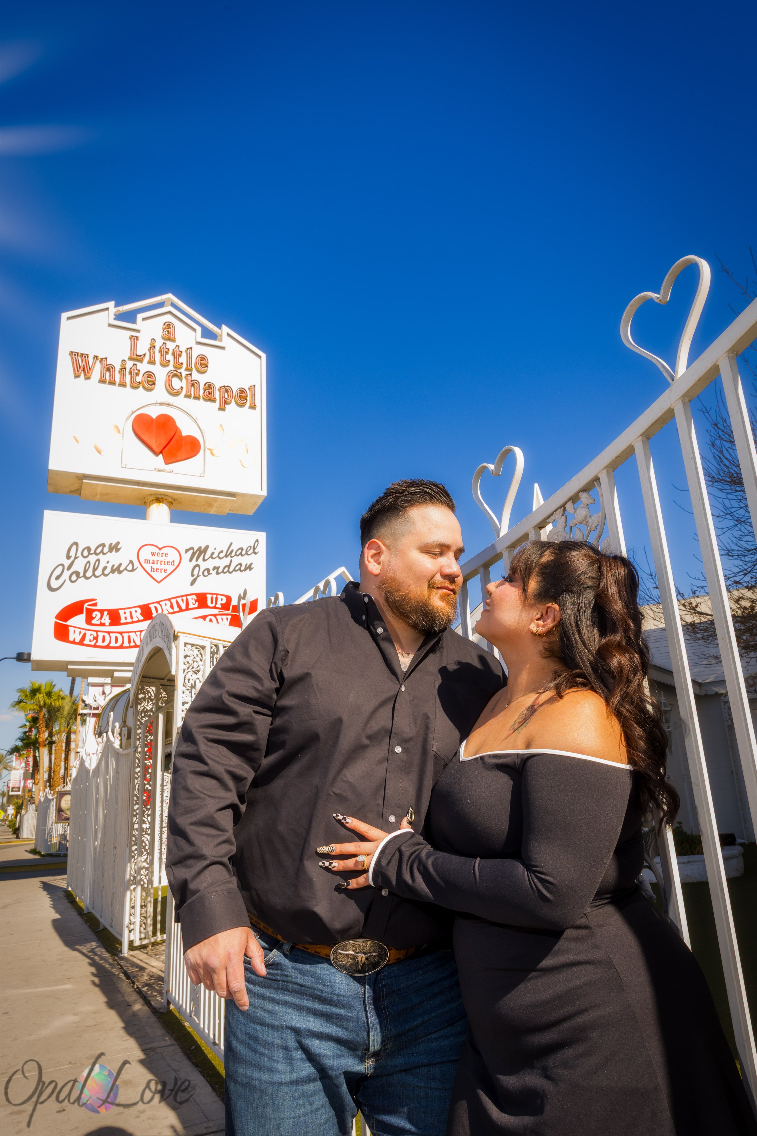 Couple embracing near the chapel entrance with decorative white heart gate behind them.