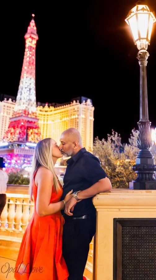 Couple kissing at Bellagio with the Eiffel Tower at Paris Las Vegas illuminated behind them.