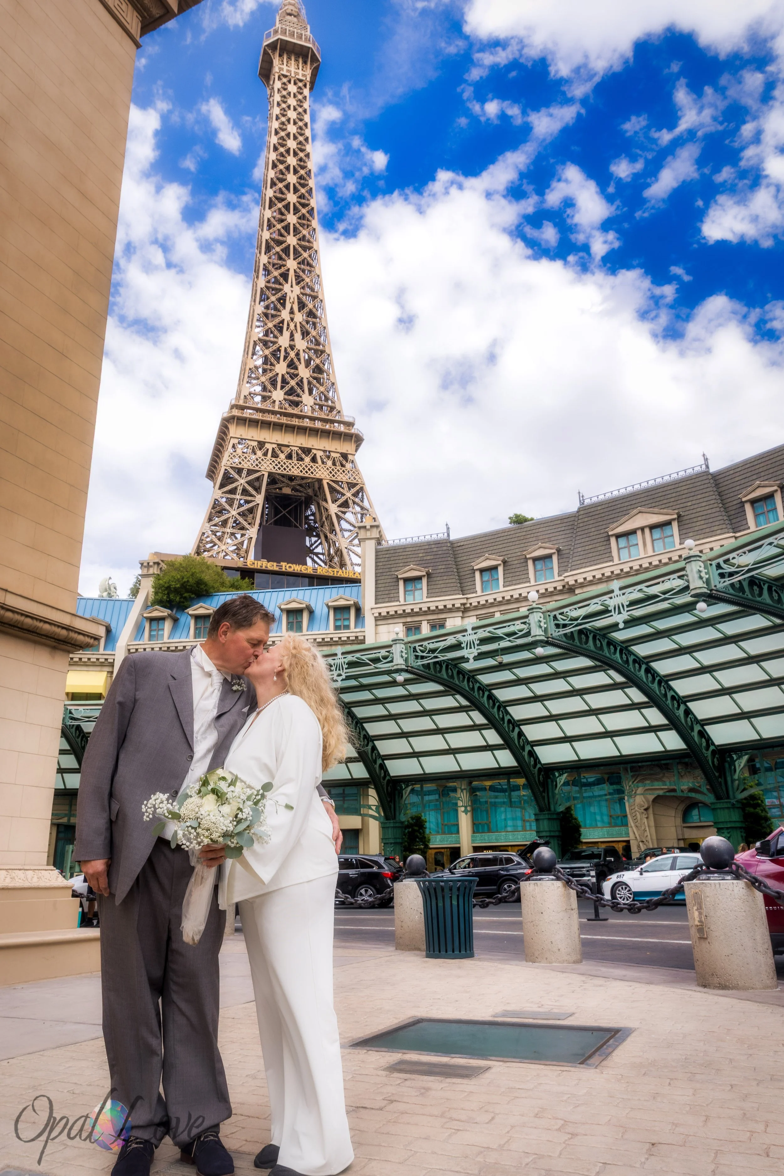 Couple kissing beneath Eiffel Tower with blue sky and clouds overhead