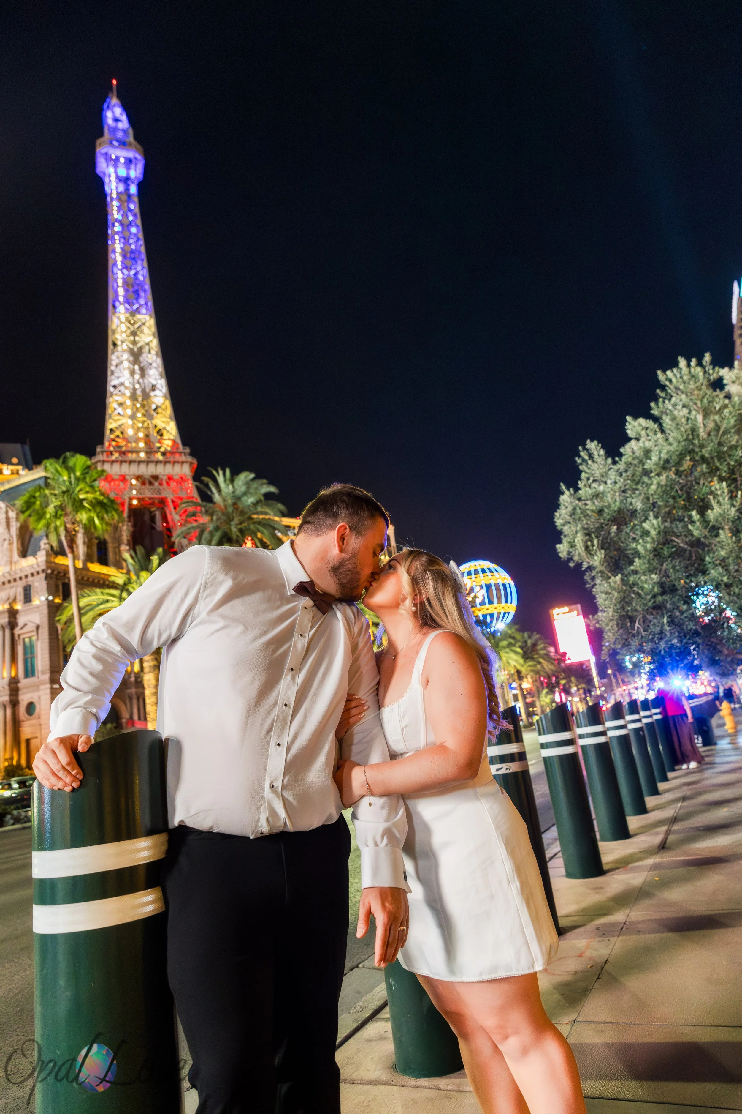 Newlywed couple sharing a kiss with Paris Las Vegas and the Las Vegas Strip lights in the background.