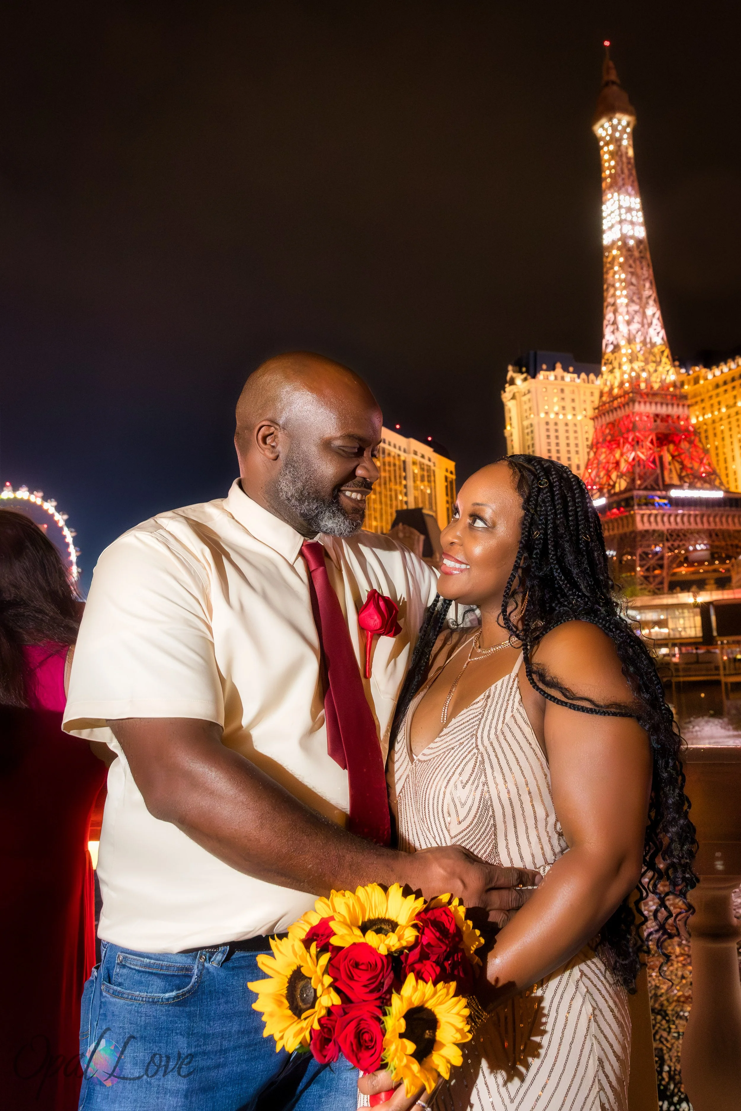 Couple smiling in front of Paris Las Vegas with Eiffel Tower lights glowing