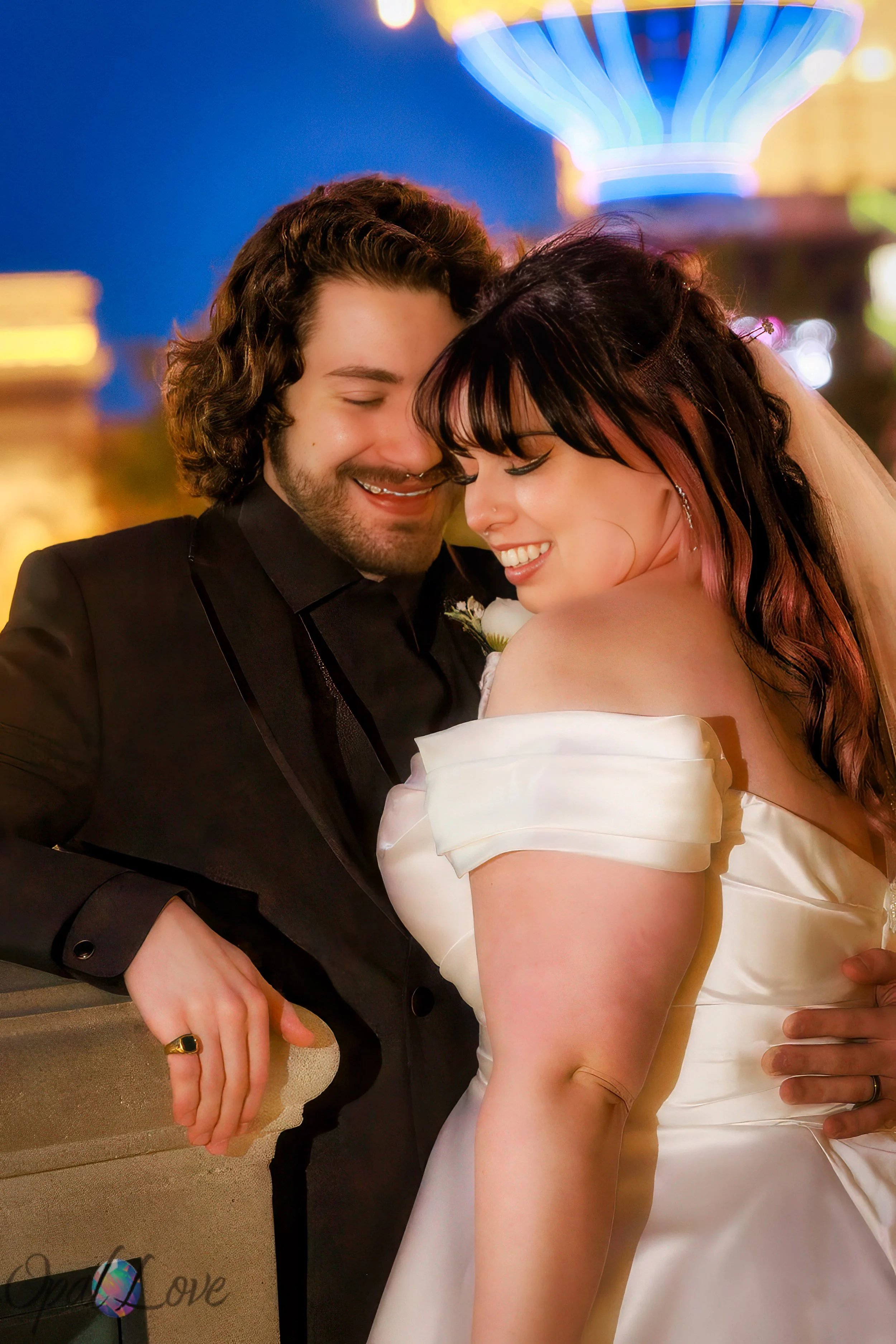 Newlyweds smiling with their heads together beneath colorful Las Vegas lights.