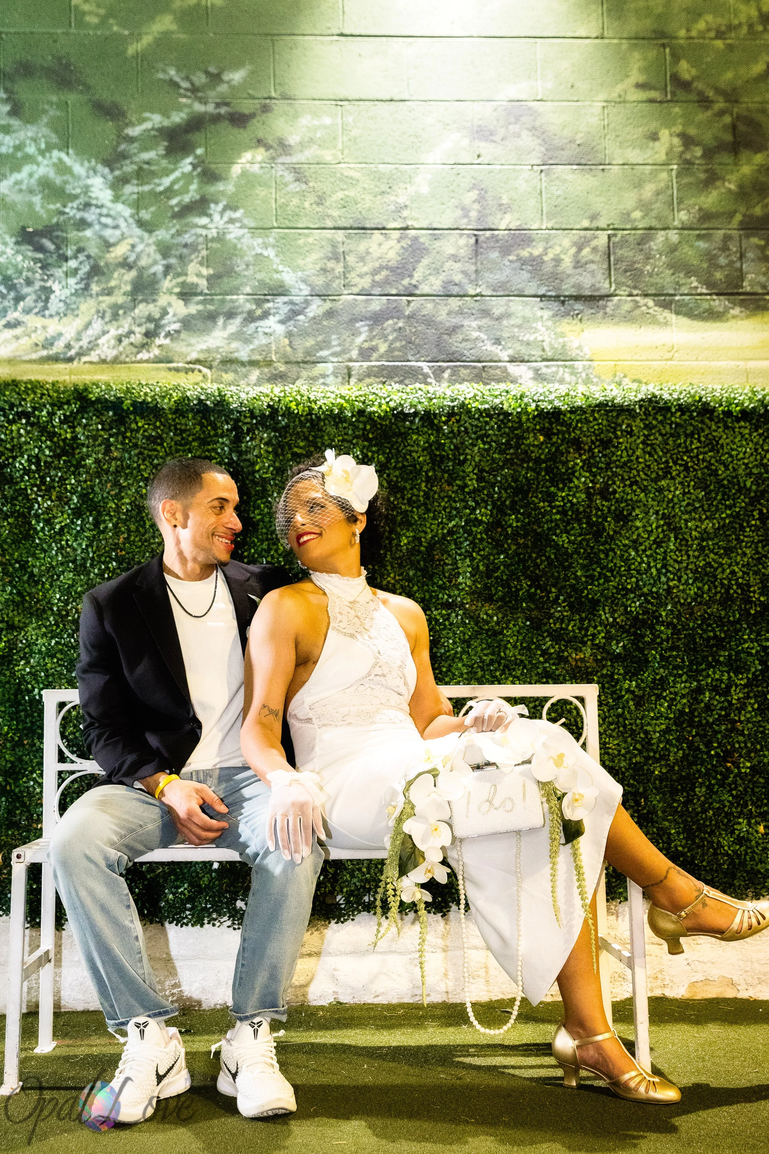 Newlyweds sitting together on a bench with greenery wall after their Las Vegas elopement ceremony.