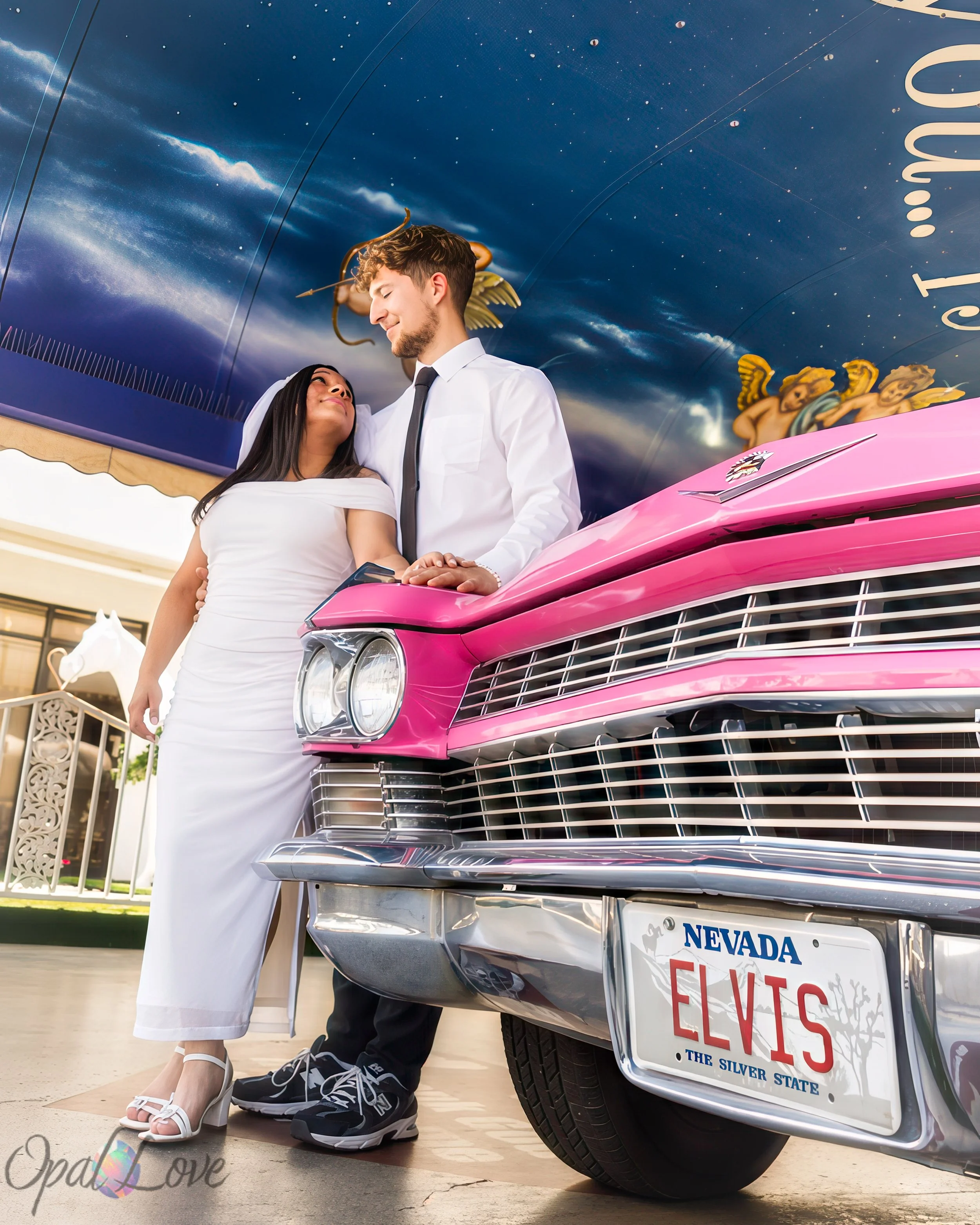 

Newlywed couple holding hands beside the pink Cadillac beneath a painted chapel canopy.