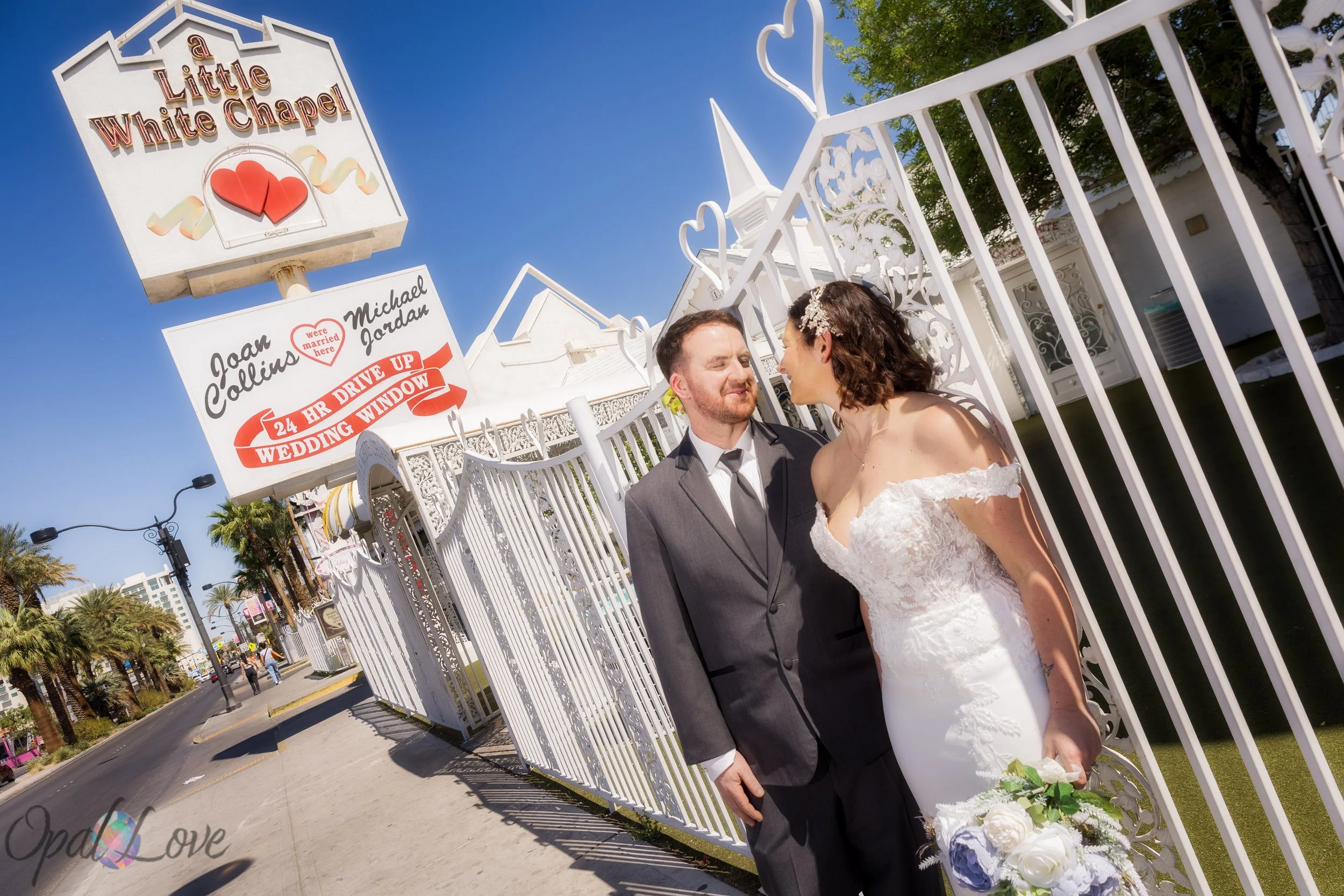 Newlywed couple posing by the Little White Chapel sign on the Las Vegas Strip after their ceremony.