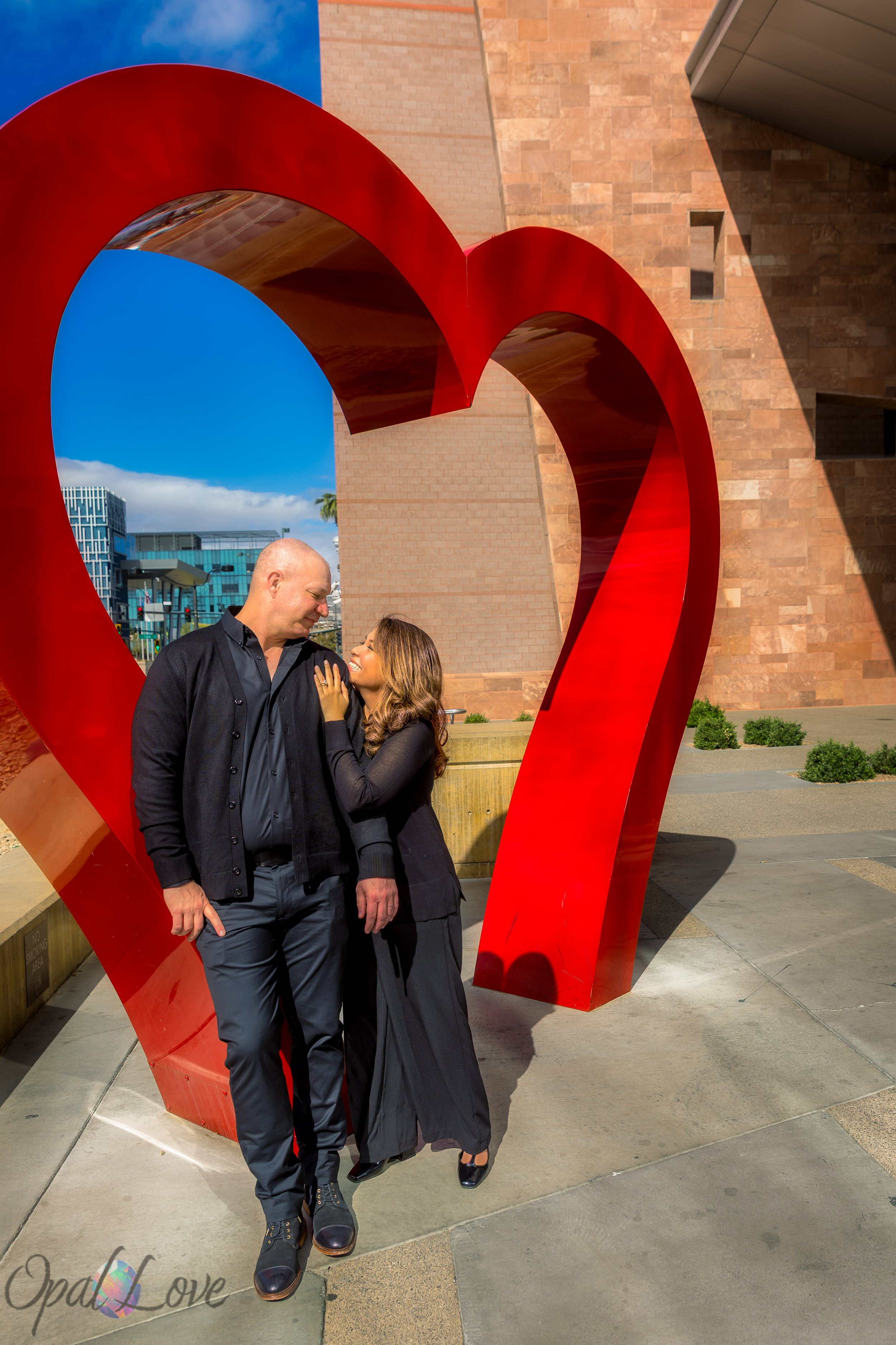 Couple dressed in black smiling together inside a large red heart sculpture in Las Vegas.