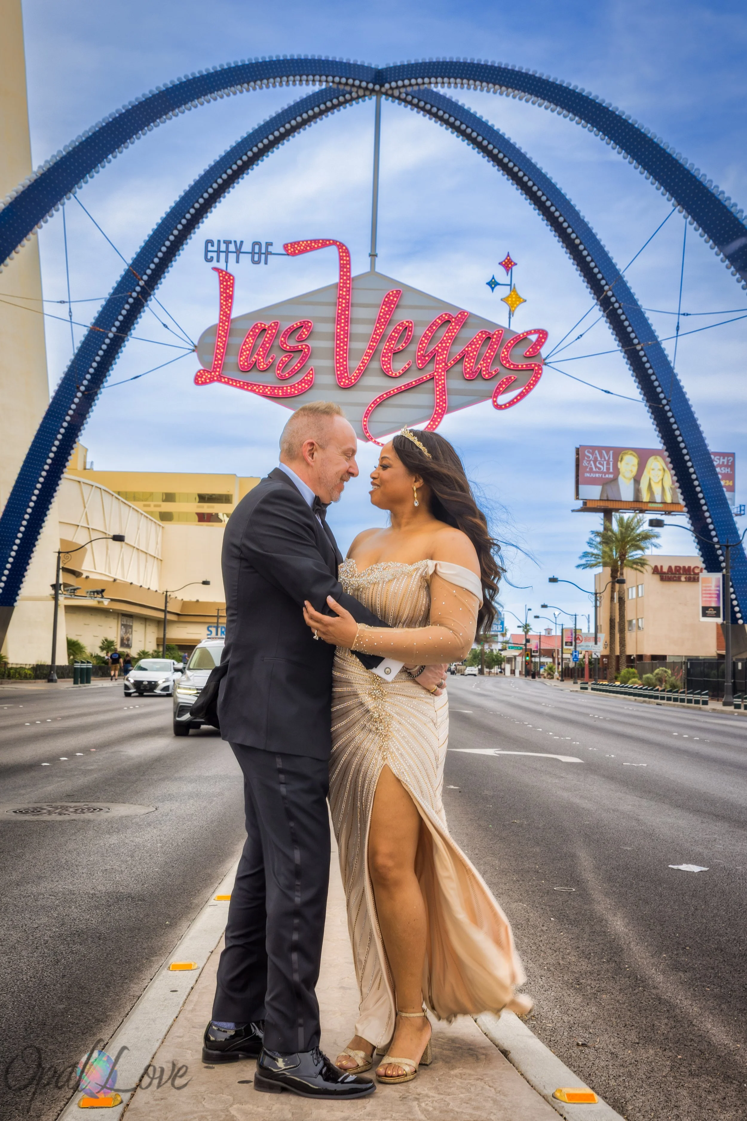 Elegantly dressed couple embraces beneath the illuminated City of Las Vegas gateway arches.
