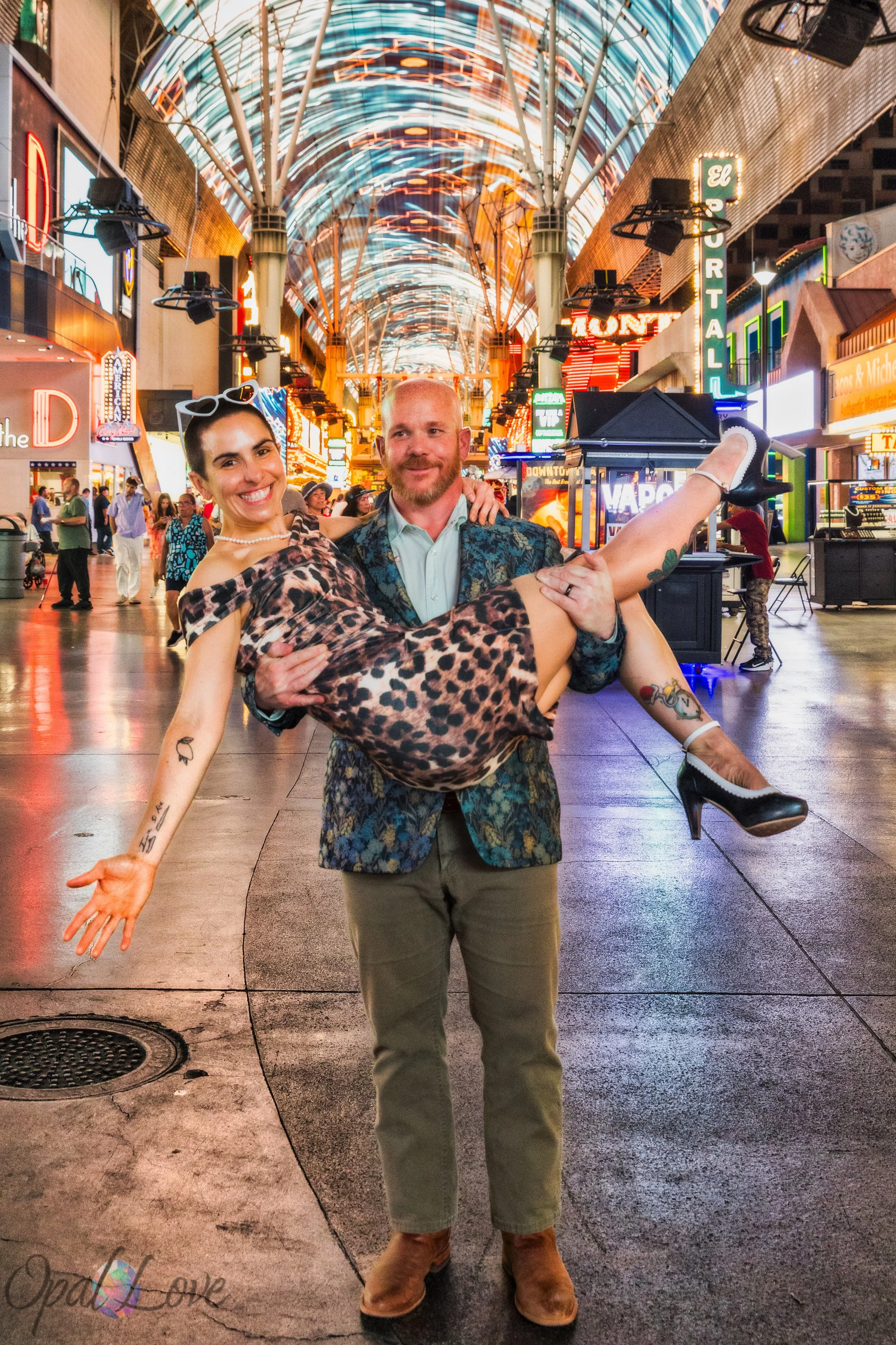 Ashley carrying Maddie during a playful couples portrait beneath the Fremont Street Experience canopy in Las Vegas.