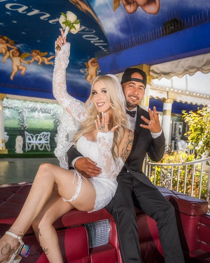 Newlywed couple showing their wedding rings on the pink Cadillac at the Little White Wedding Chapel in Las Vegas.