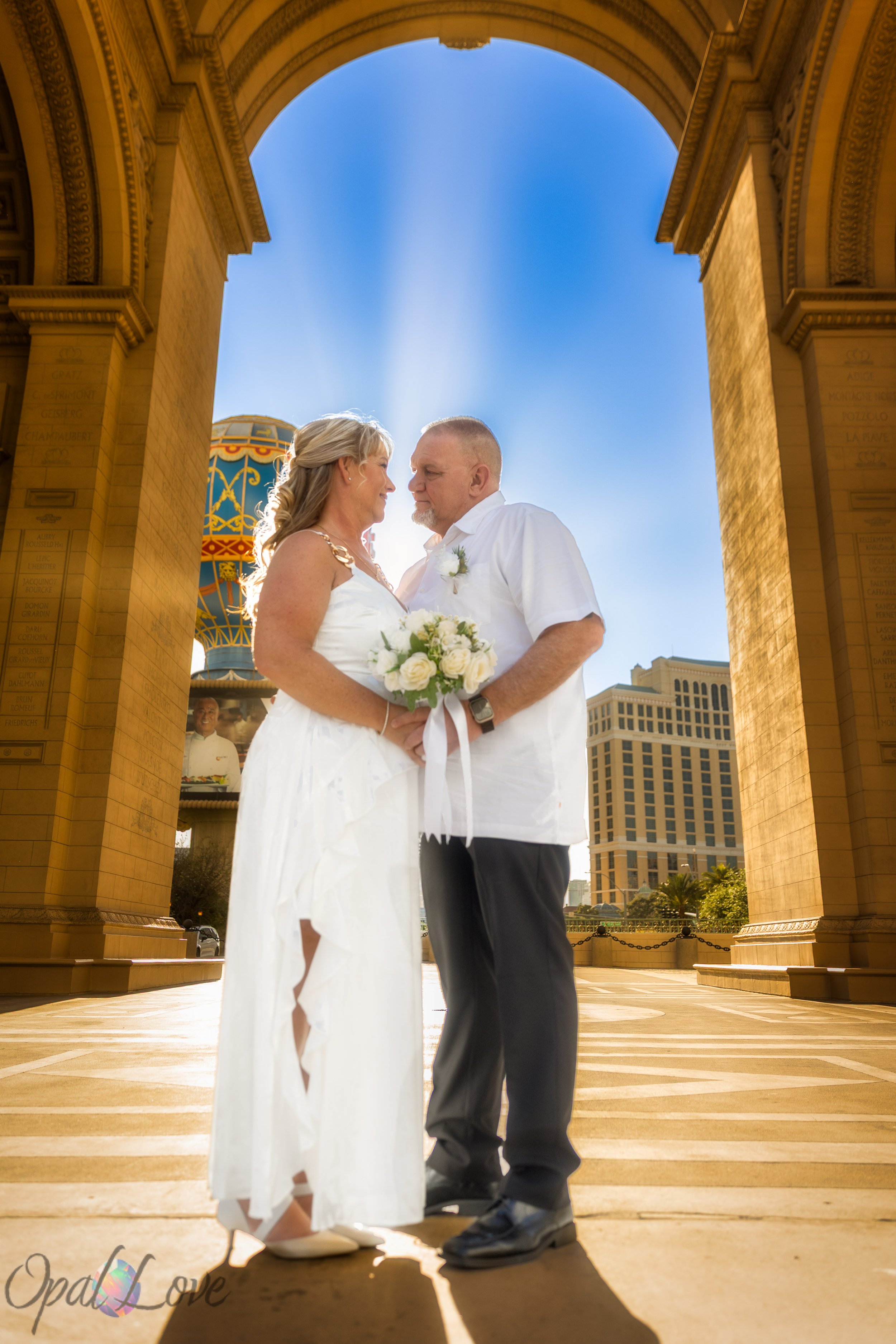 Bride and groom standing together under the Bellagio arch with blue sky during their Las Vegas Strip portraits.