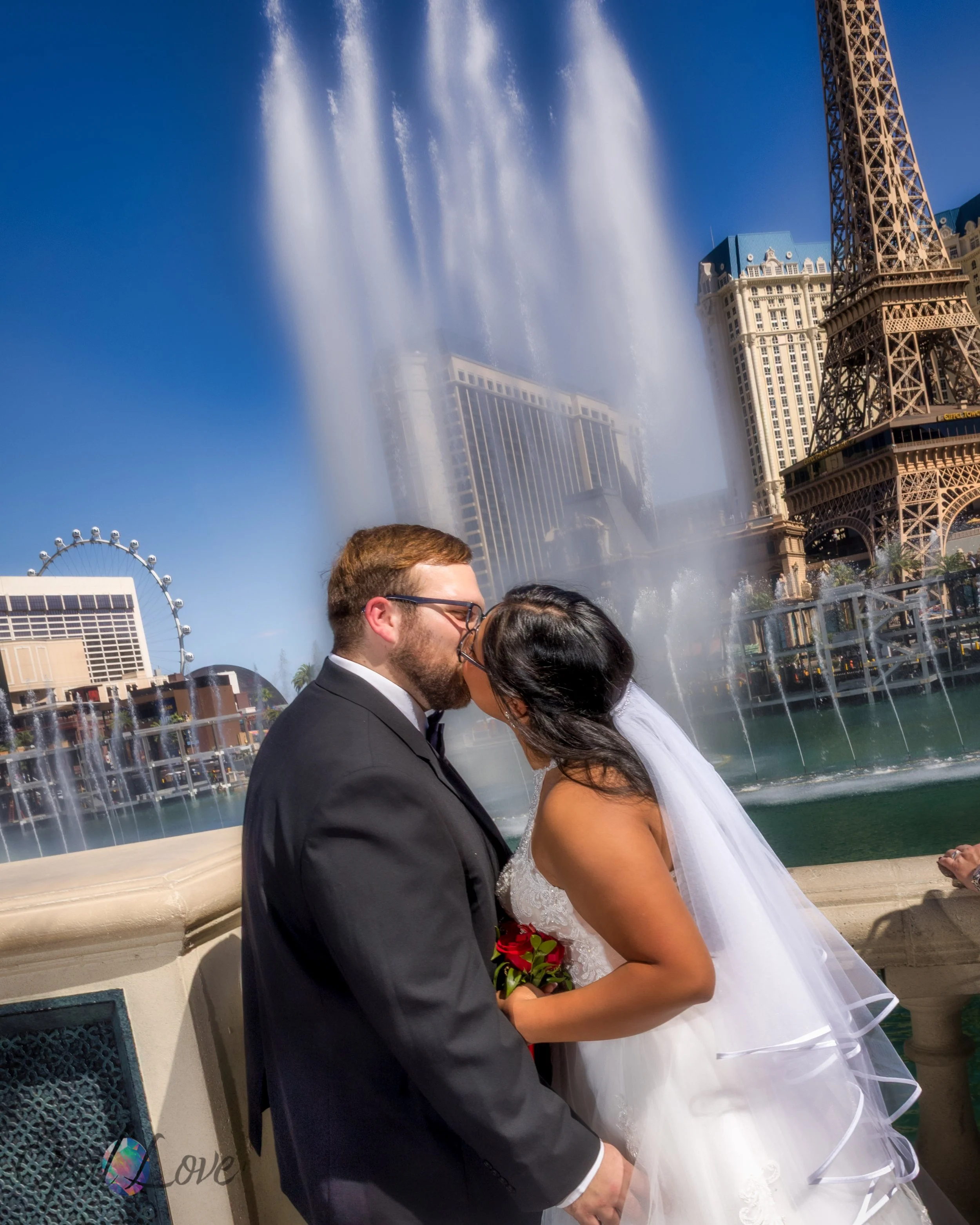Newlyweds kissing by the Bellagio fountains with Paris Las Vegas skyline in view.