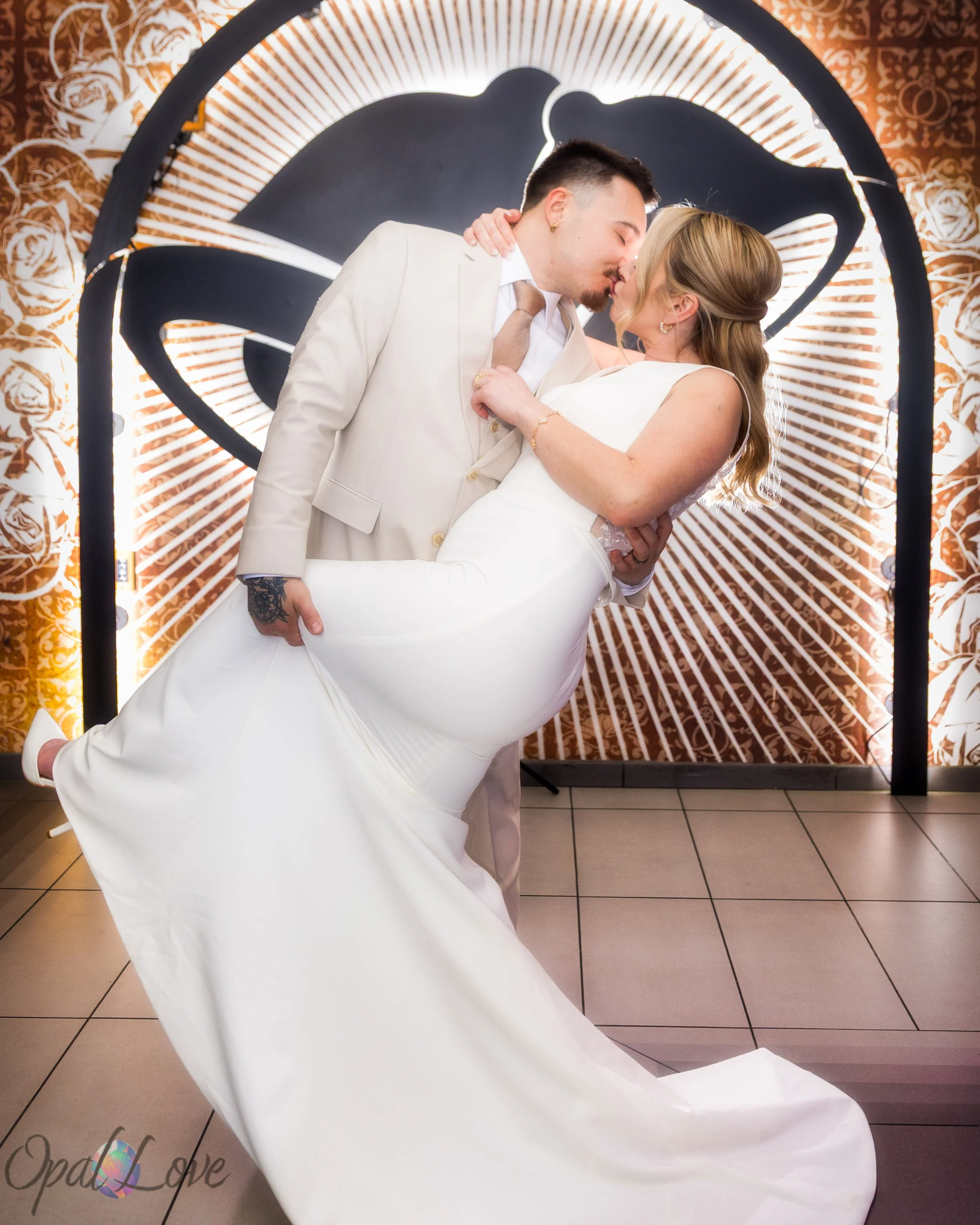 Groom dipping the bride for a kiss in front of a glowing circular swan backdrop.