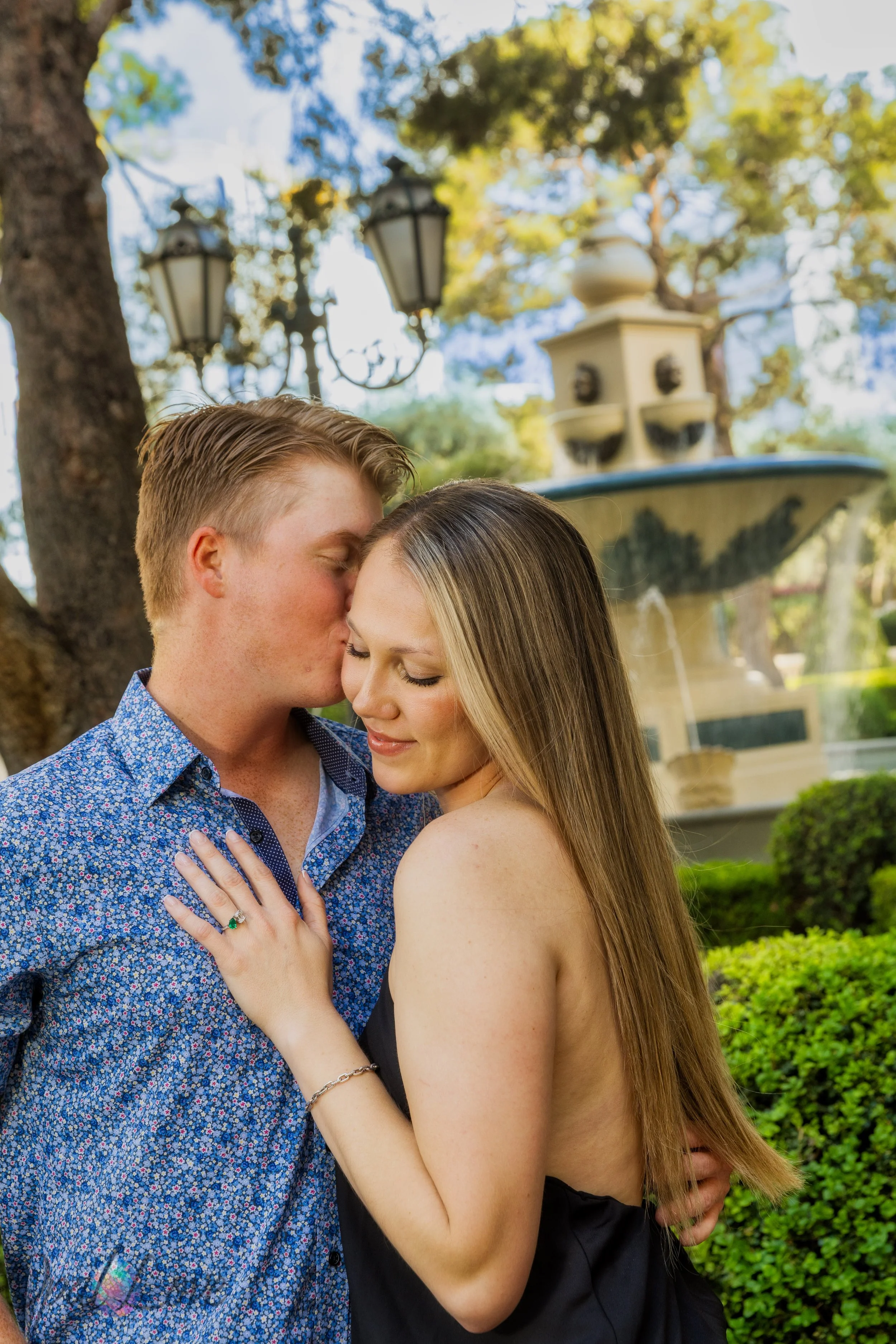Newly engaged couple embracing near Bellagio gardens with fountain backdrop