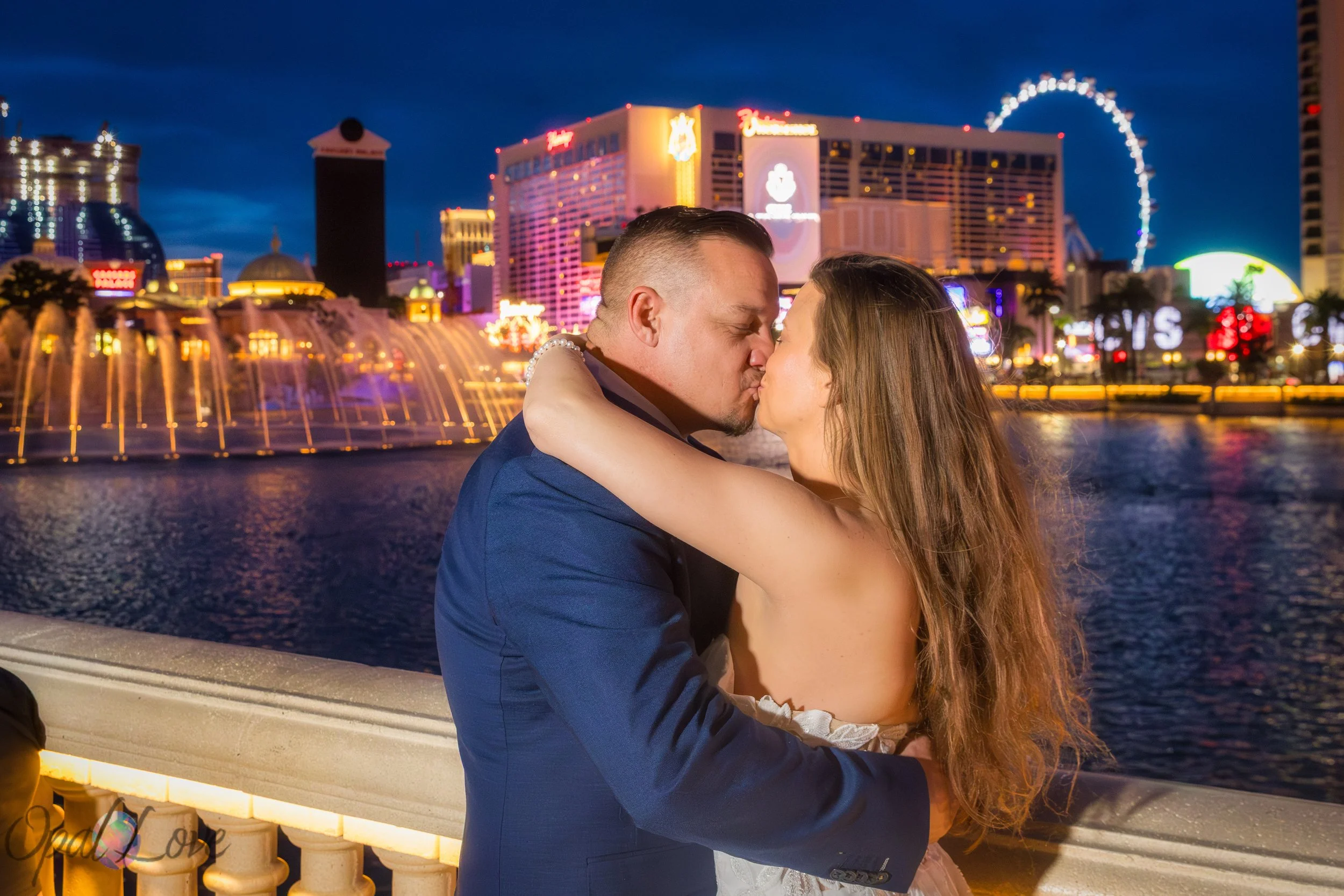 Bride and groom kissing in front of the Bellagio fountains with Las Vegas Strip lights at night.