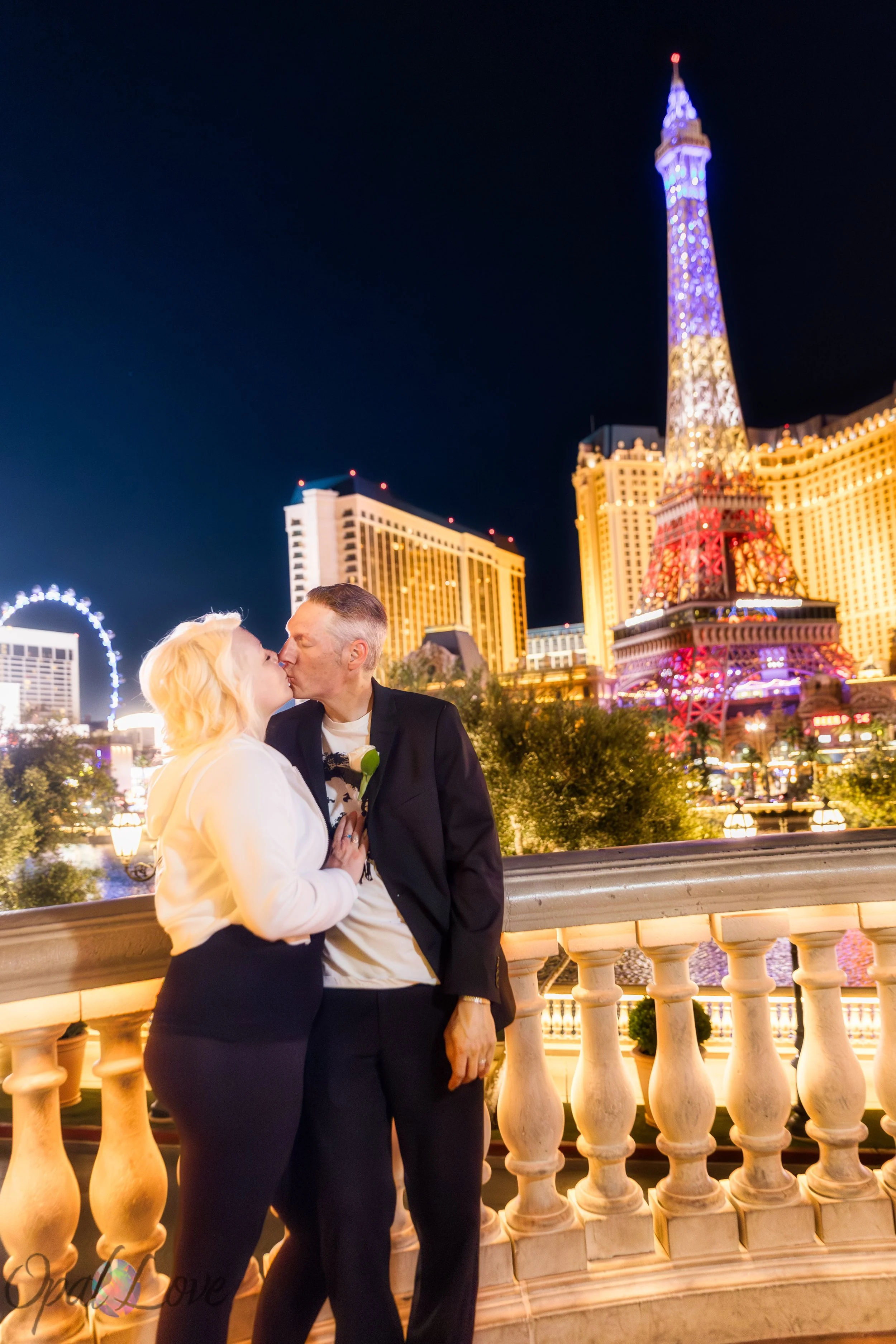 Wide shot of couple kissing on a balcony overlooking the Las Vegas Strip and Paris Las Vegas