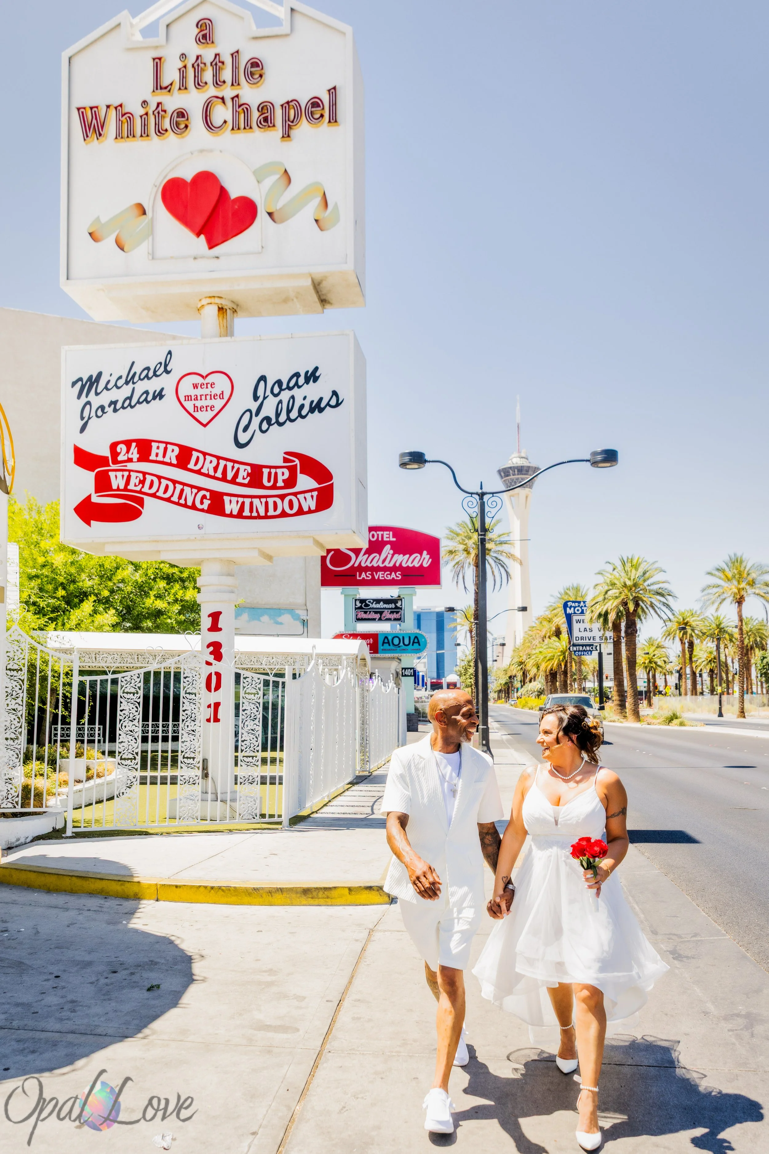 Newlyweds Stephanie and Jacent walking together beside the vintage Little White Wedding Chapel sign on Las Vegas Boulevard.