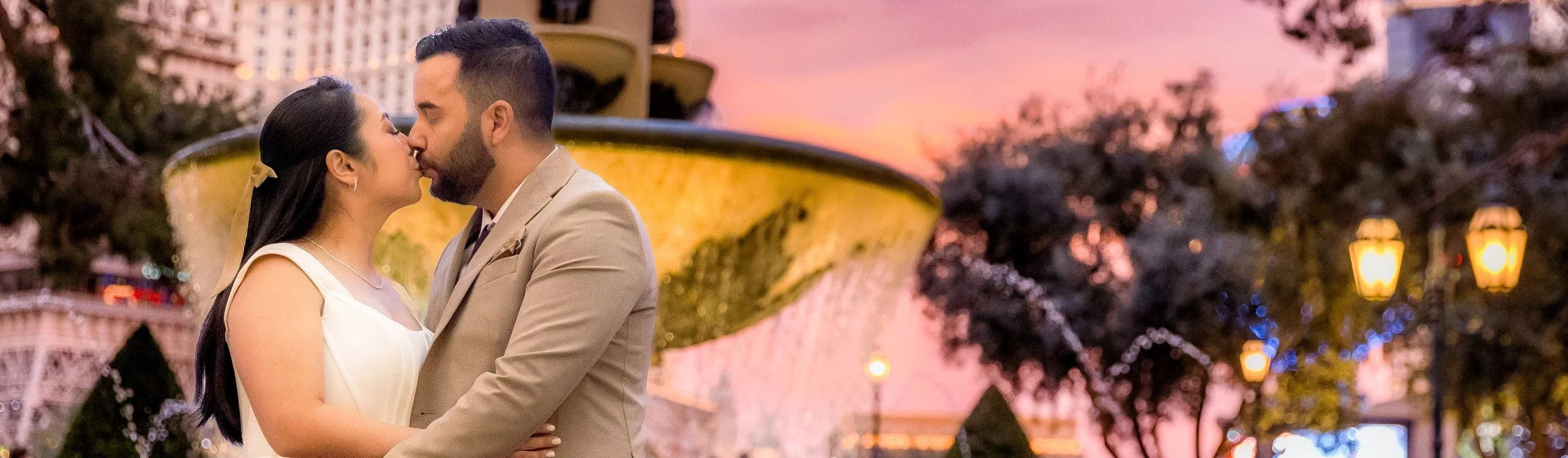 Wedding couple kissing beside a purple-lit fountain on the Las Vegas Strip at night.