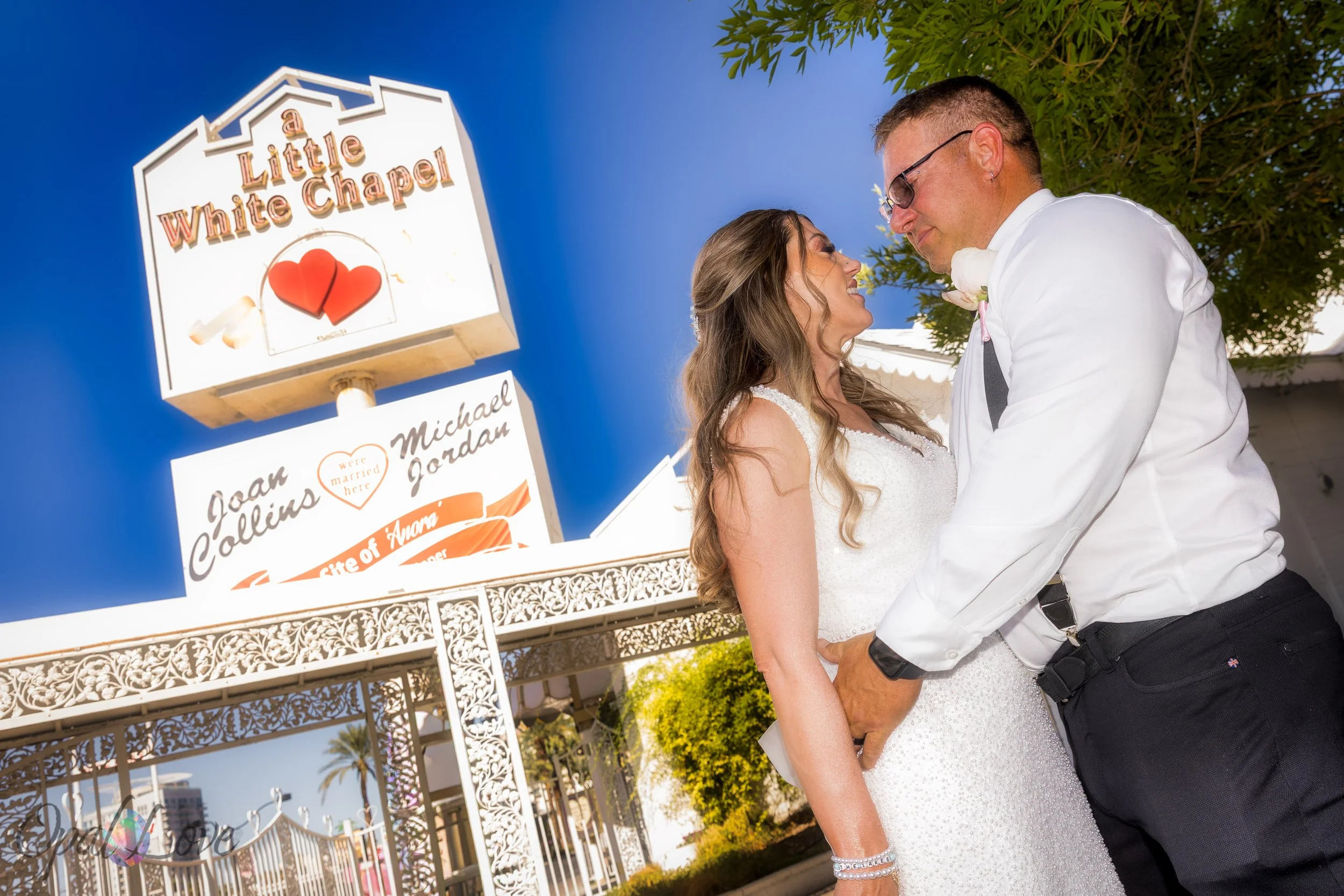 Couple smiling beneath Little White Wedding Chapel heart sign in Las Vegas.