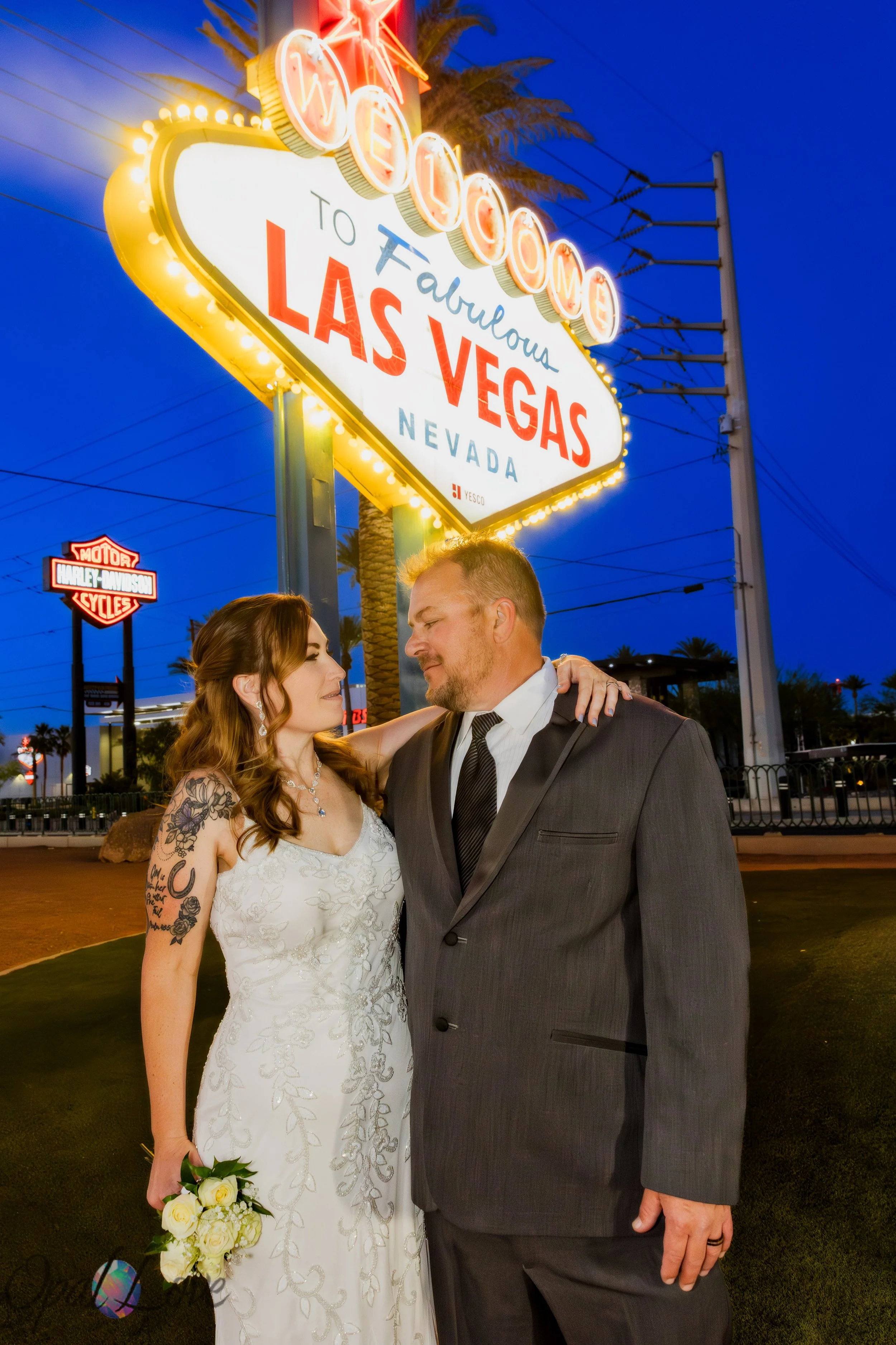 Bride and groom standing beneath the illuminated Welcome to Fabulous Las Vegas sign at sunset.
