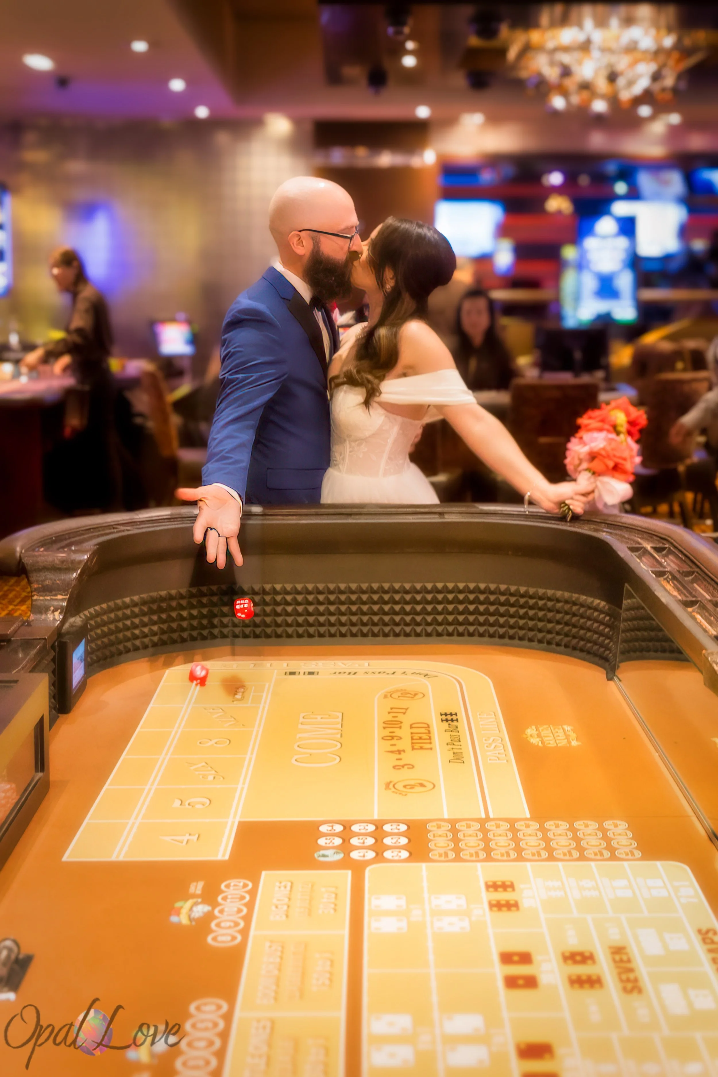 Newlyweds kiss beside a craps table on a classic Las Vegas casino gaming floor.