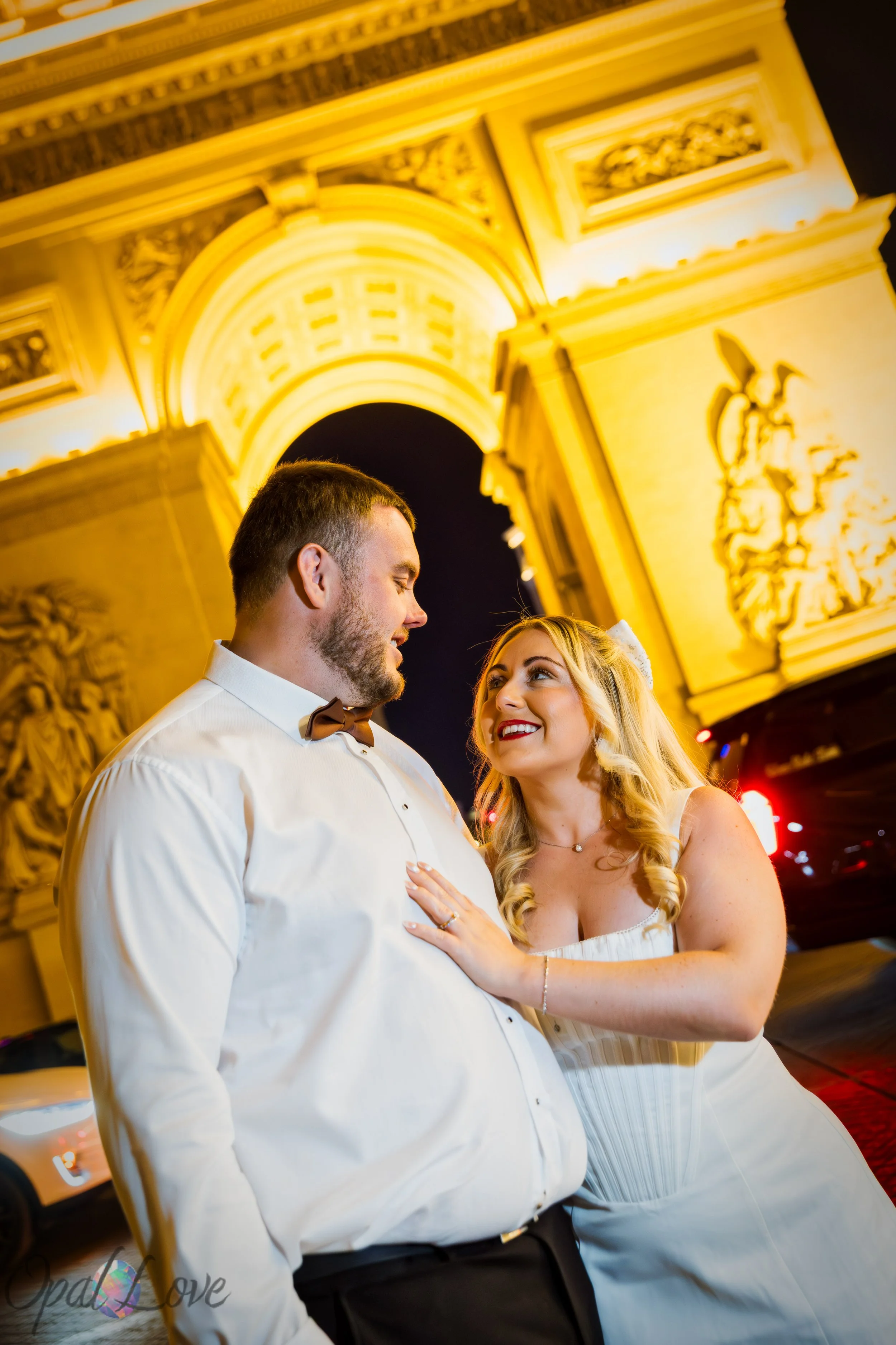Newlywed couple in wedding attire beneath the illuminated Eiffel Tower at Paris Las Vegas at night.