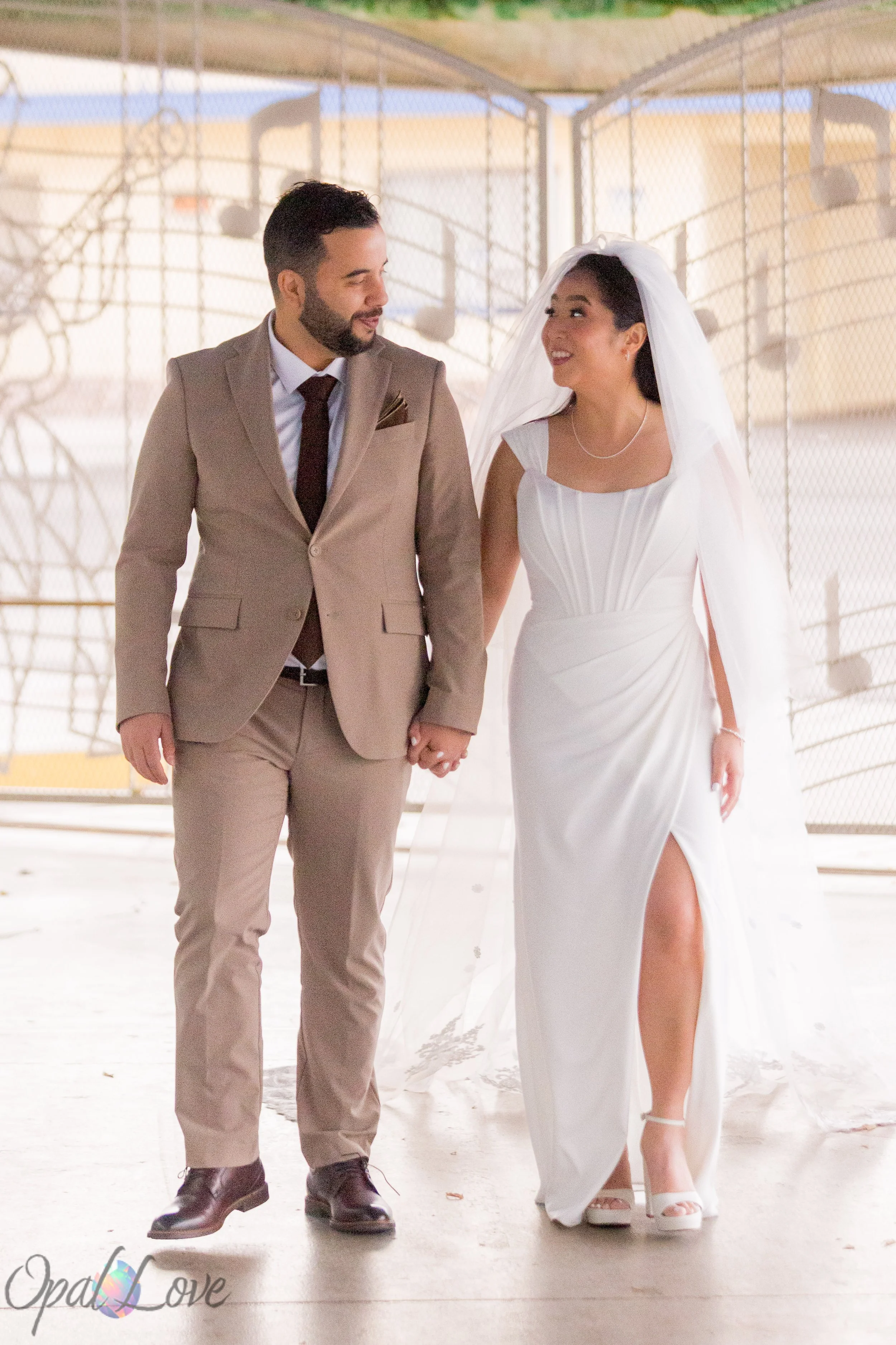 Newlyweds walking hand in hand beneath a white garden pavilion.