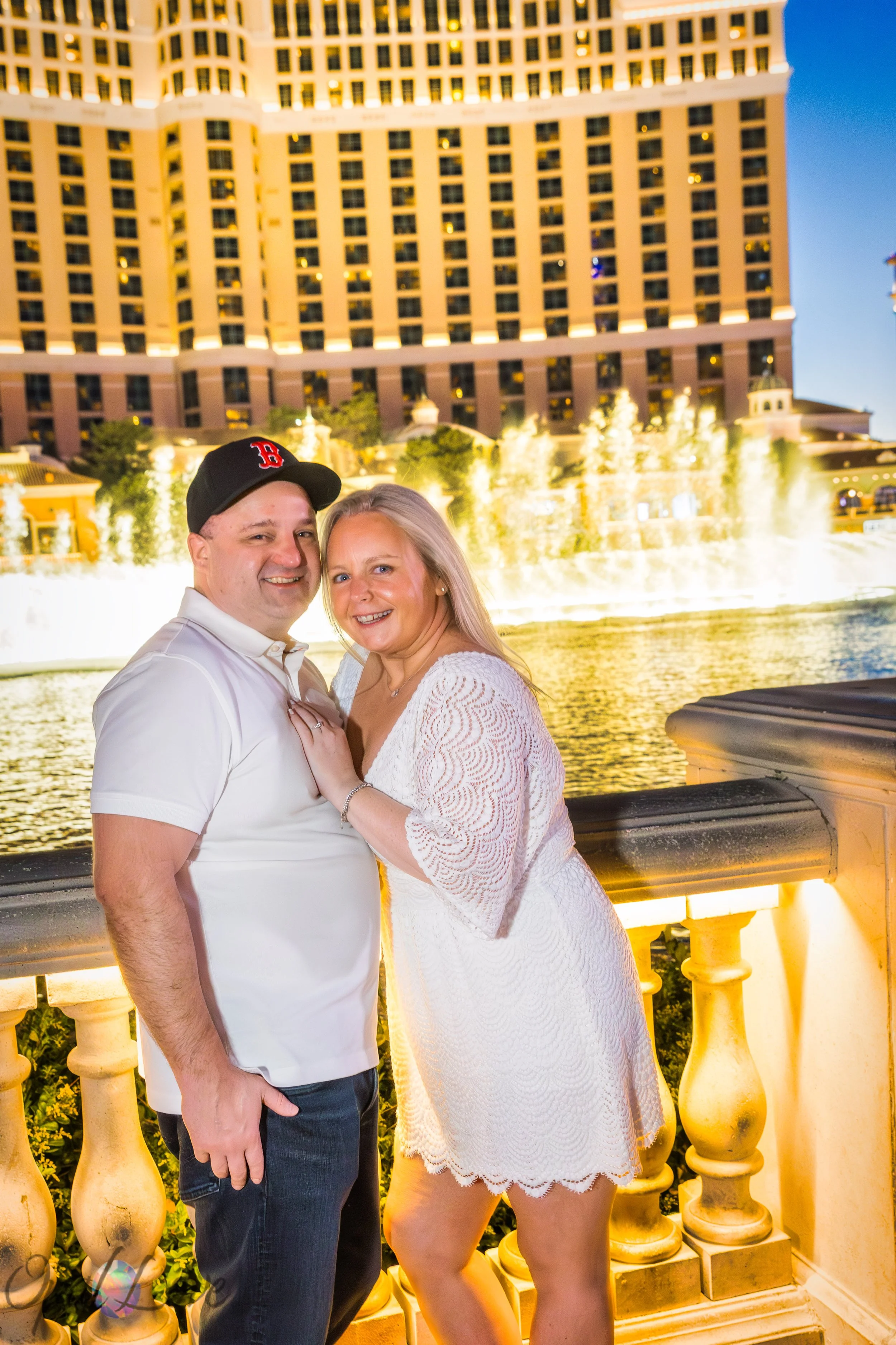 Couple smiling together in front of the Bellagio fountains at night.