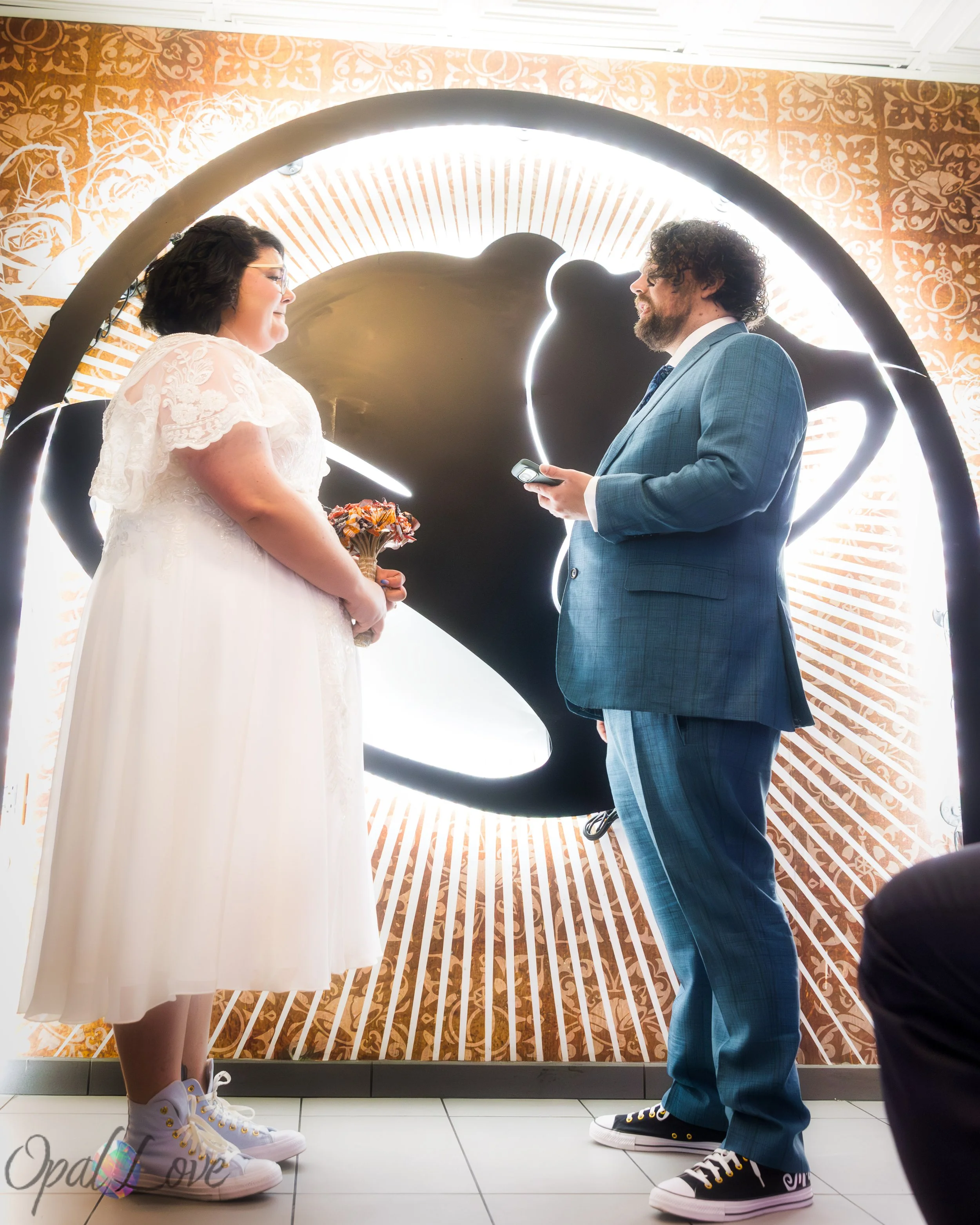 Groom reading from a sheet of paper during the ceremony, facing the bride in front of a glowing swan backdrop.