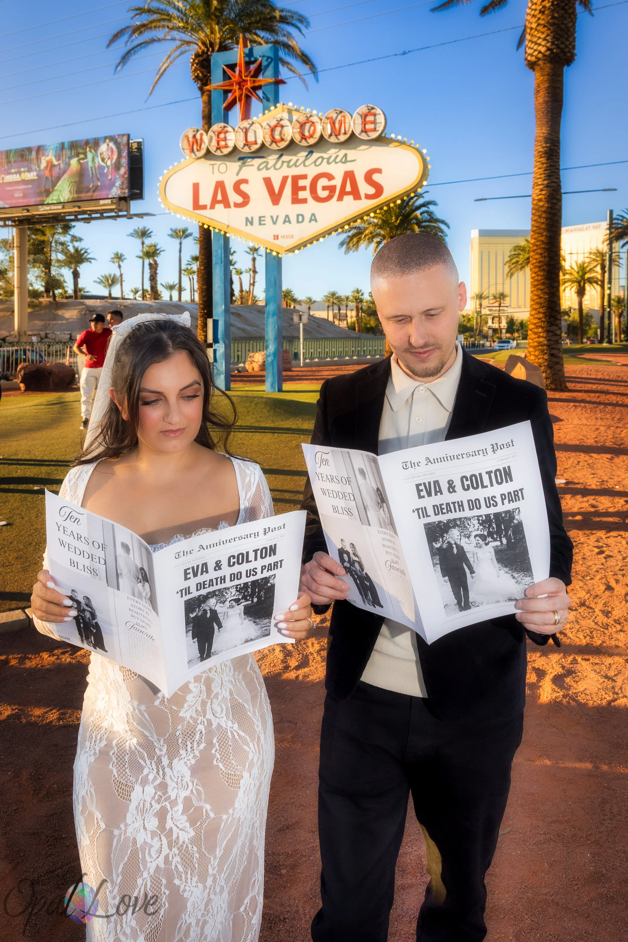 Couple reading custom anniversary newspapers while standing beneath the Welcome to Las Vegas Sign.