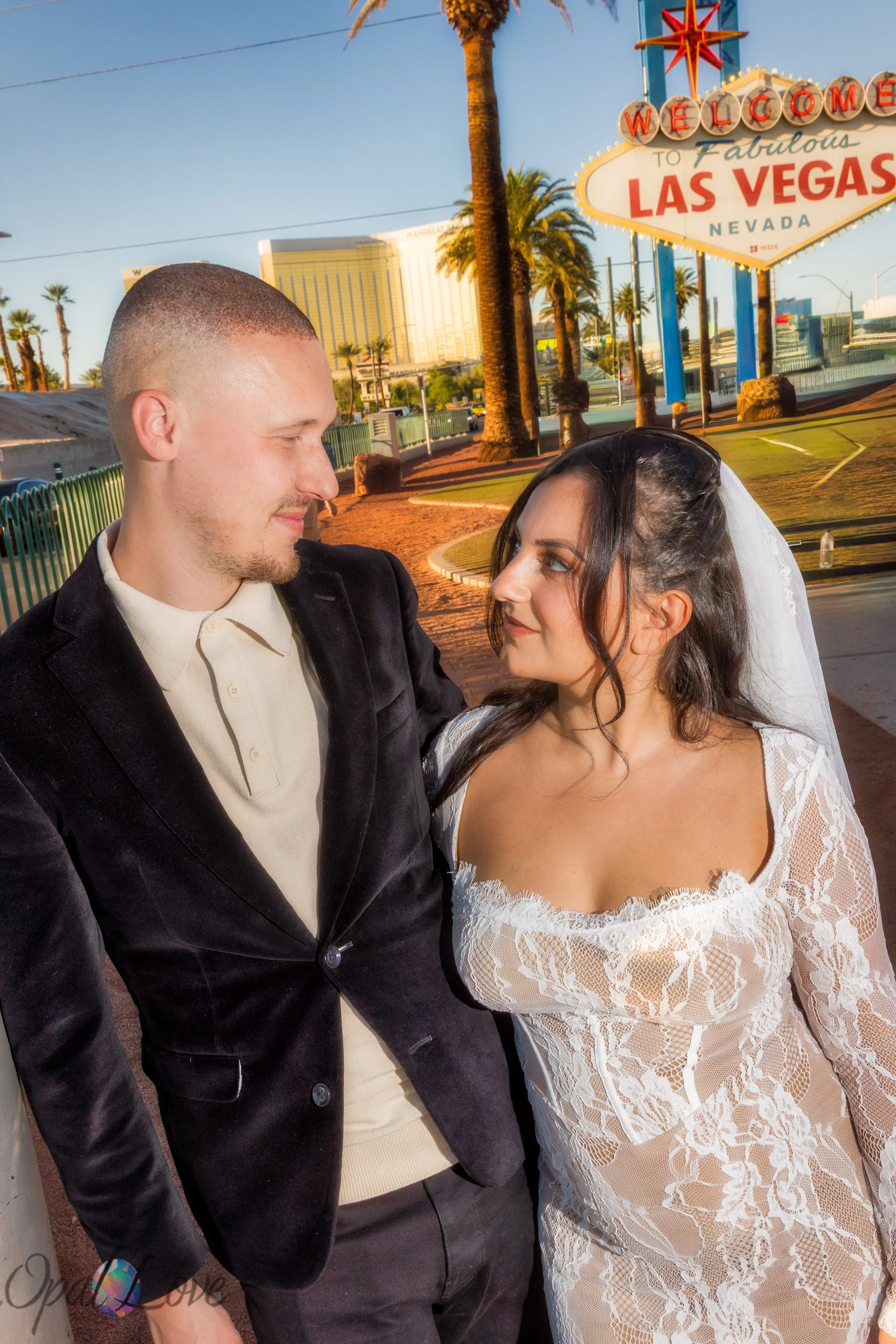 Close up of the couple looking at one another with palm trees and the Las Vegas Sign in the background.