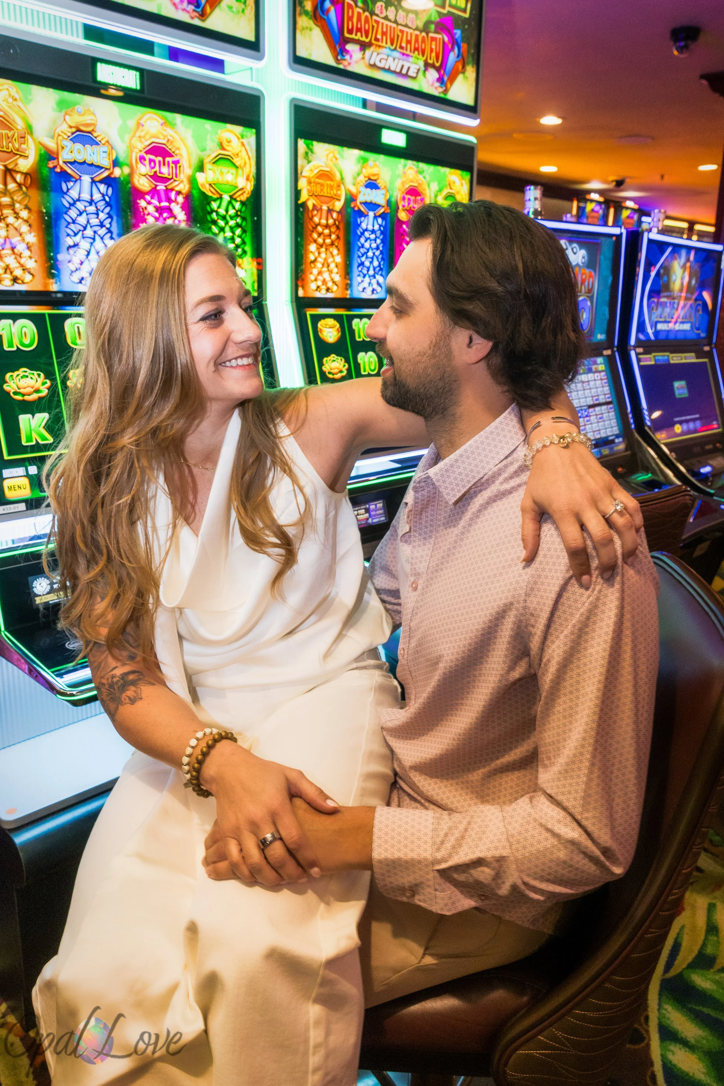 Newly engaged couple sitting together in front of bright slot machines inside a Fremont Street casino during their Las Vegas engagement photo session.