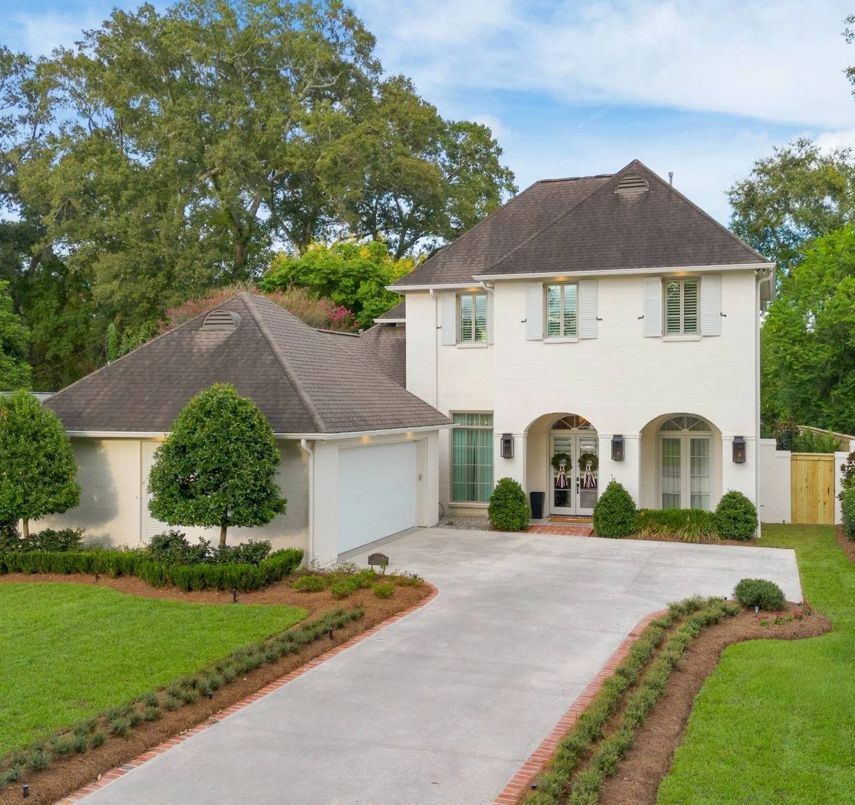 White brick home with an arched entry, clipped hedges and a concrete driveway — Flora Landscape Contractors