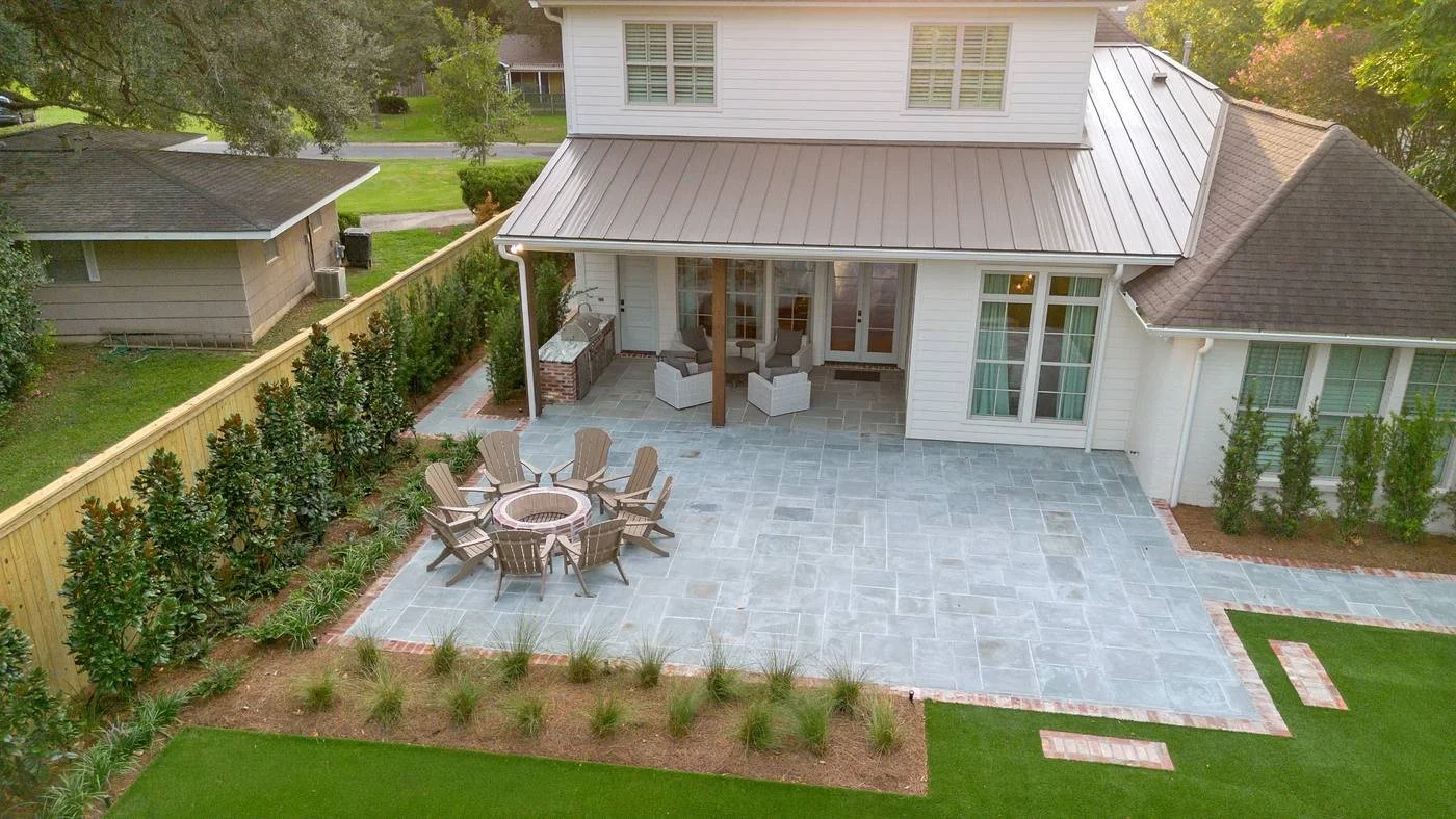 Bluestone terrace off the covered patio with a fire pit and fence-line magnolias — Flora Landscape Contractors