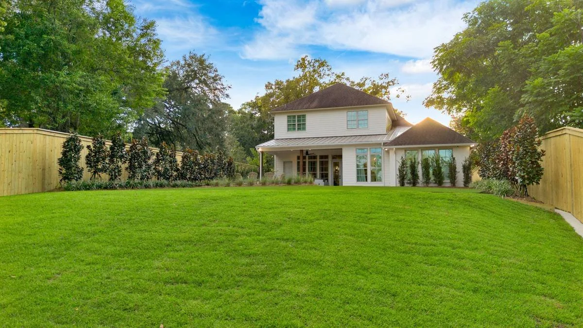 Sloped sod lawn behind the home with plantings along both fence lines — Flora Landscape Contractors