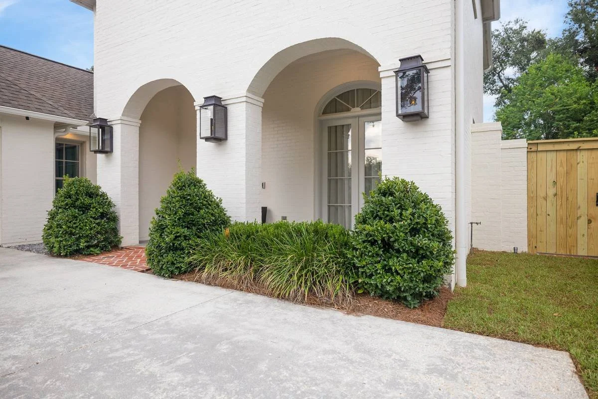 Rounded shrubs planted along the arched entry of a white brick home — Flora Landscape Contractors