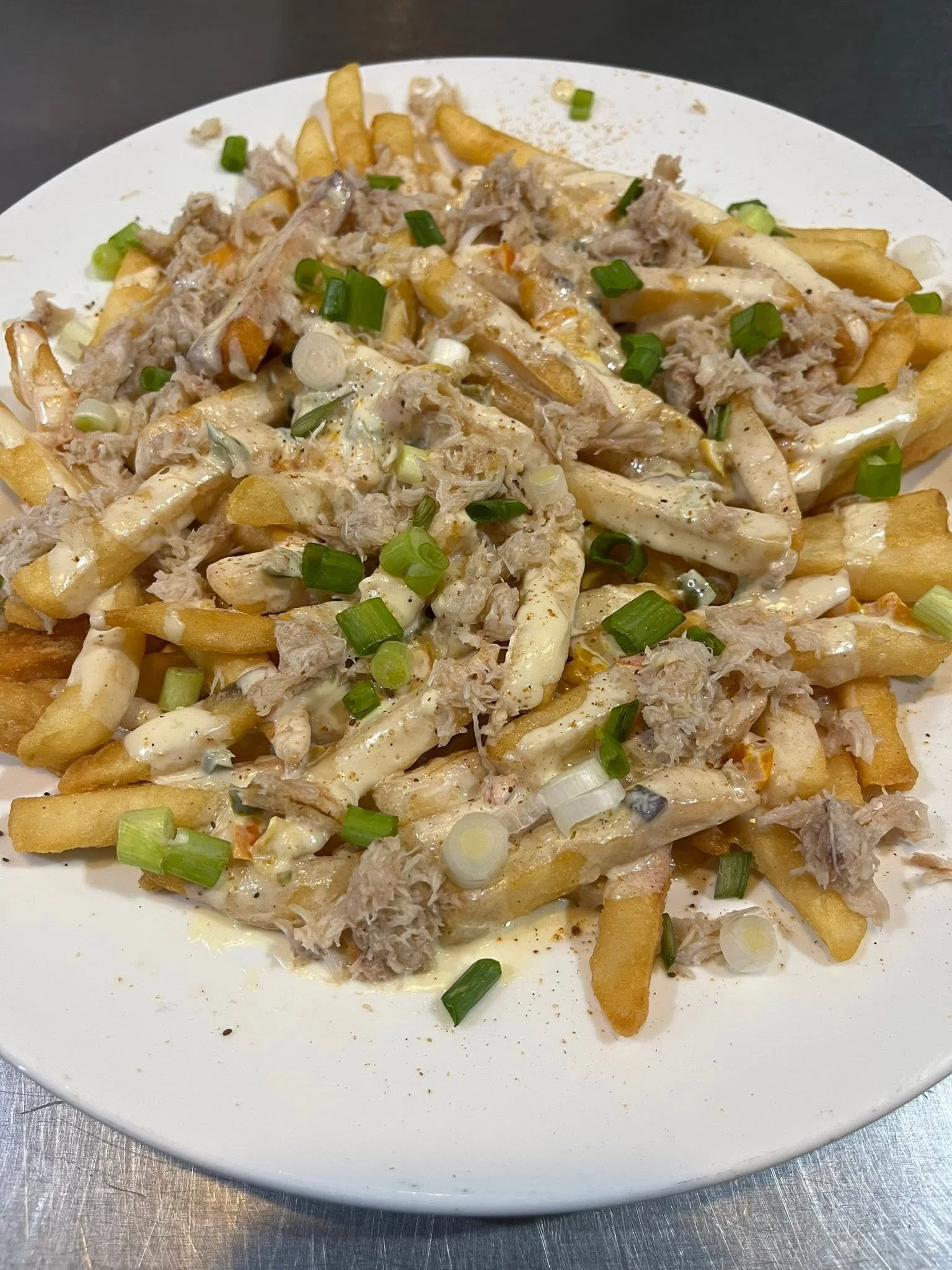 Plate of French fries topped with shredded chicken, creamy sauce, chopped green onions, and seasonings.