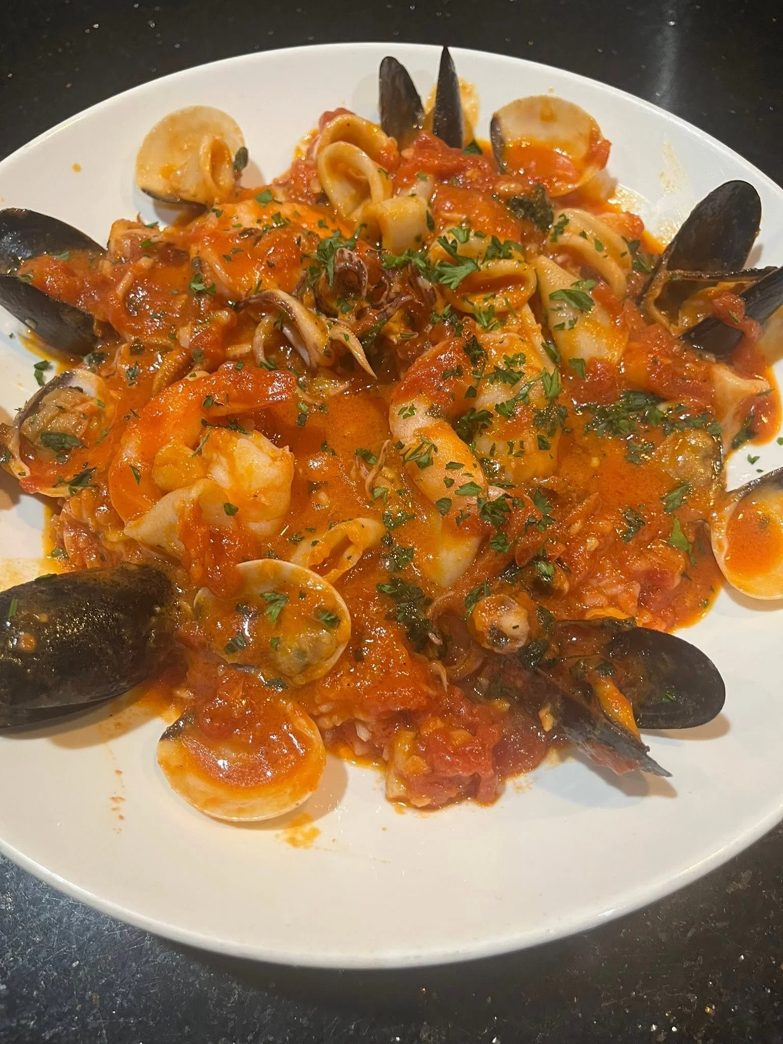 Plate of seafood pasta with shrimp, mussels, and chopped herbs in tomato sauce.